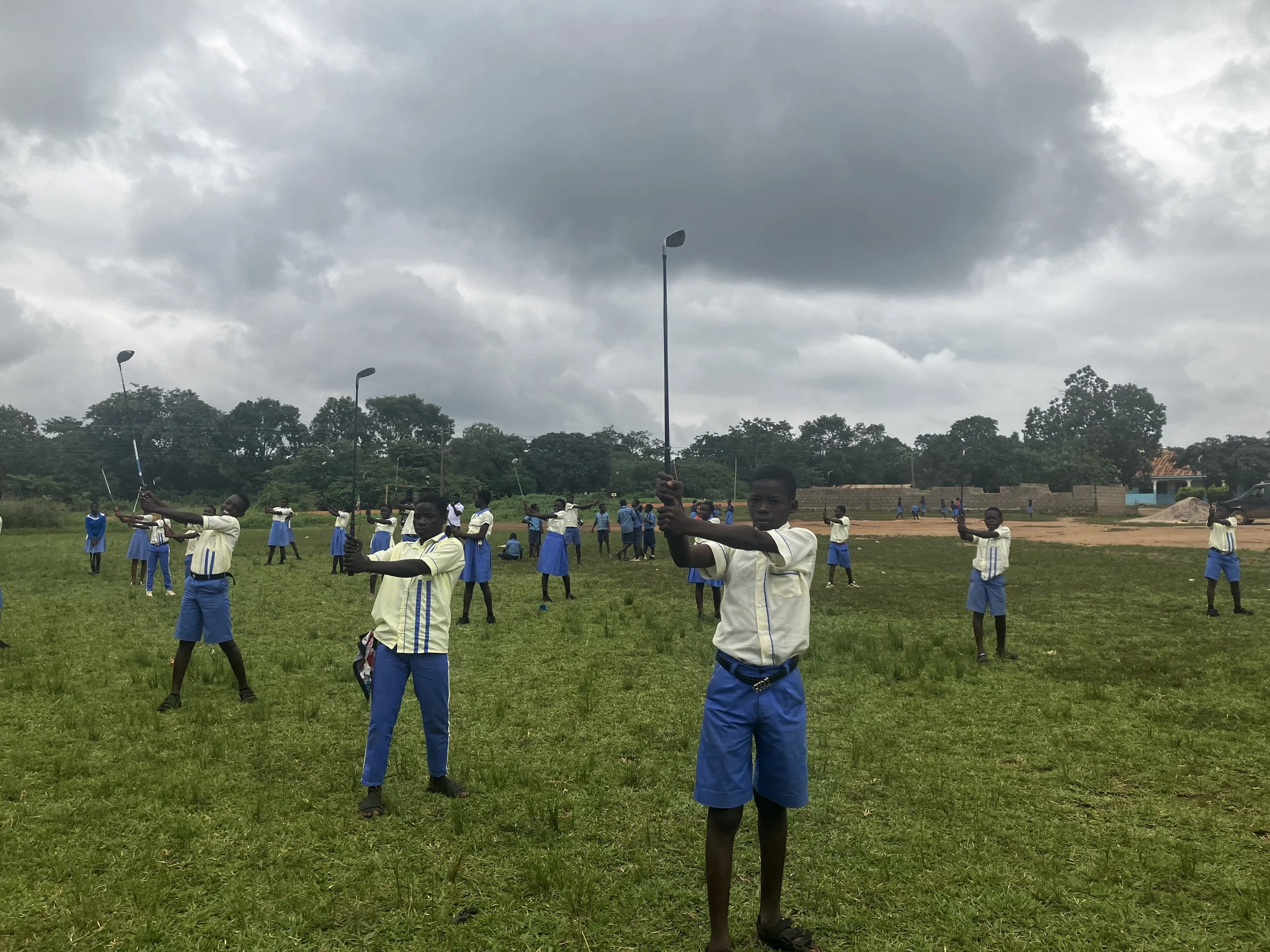 Group of students practicing golf on a grassy field under cloudy sky.