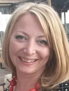 A smiling woman with blonde hair, wearing a red necklace and black top.