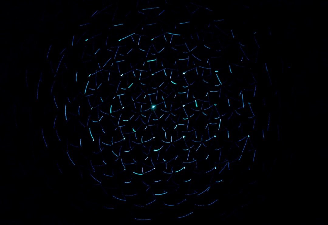 Dark image with numerous small, glowing, curved lines in shades of blue and cyan, arranged in a swirling pattern.