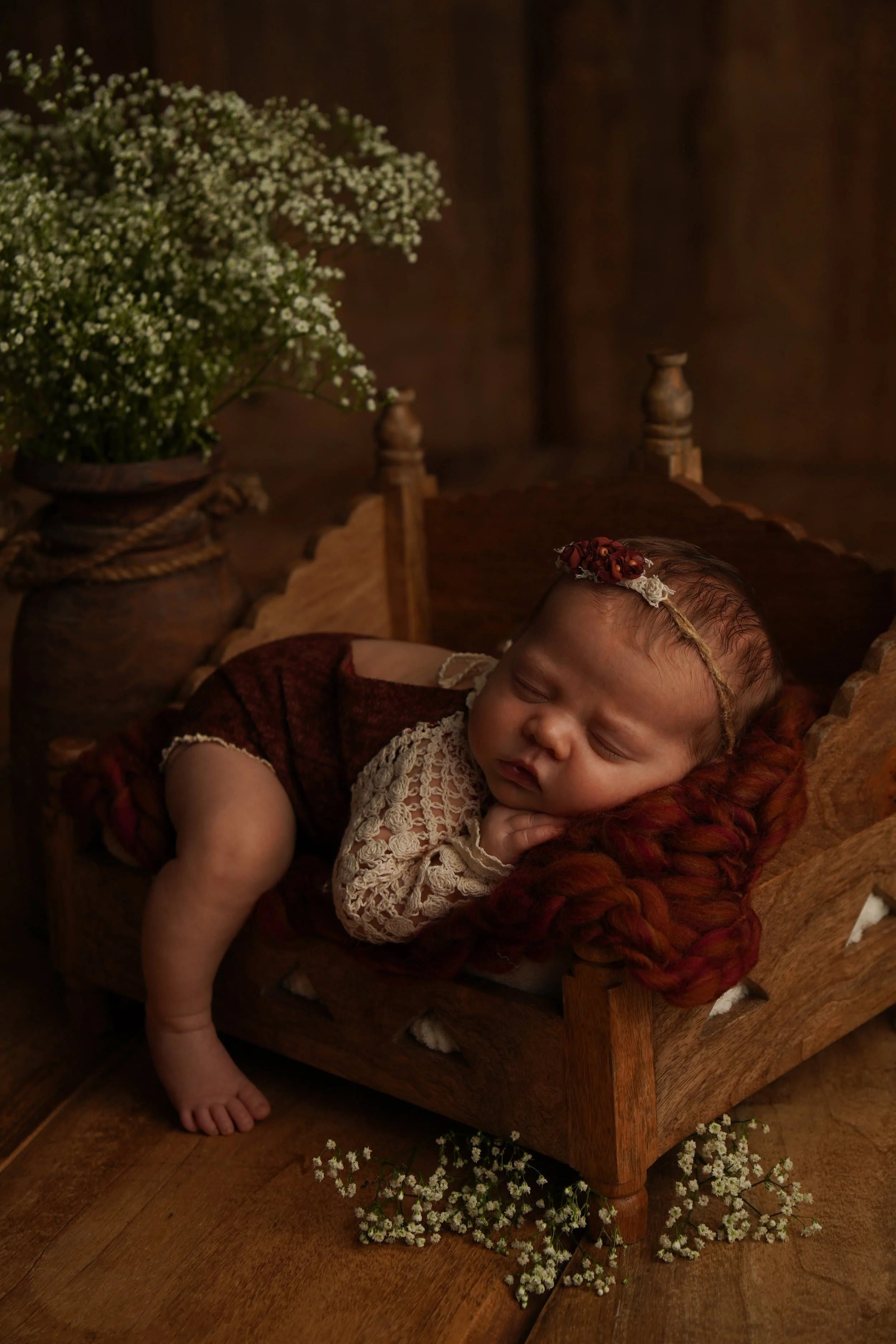 Ein kleines Baby schläft auf einem kleinen Holzbett, umgeben von Blumen und einer rustikalen Umgebung. KaysserArt Fotografie Rottweil Robert Kaysser Fotograf, Neugeborenenfotograf, Babybauchfotograf