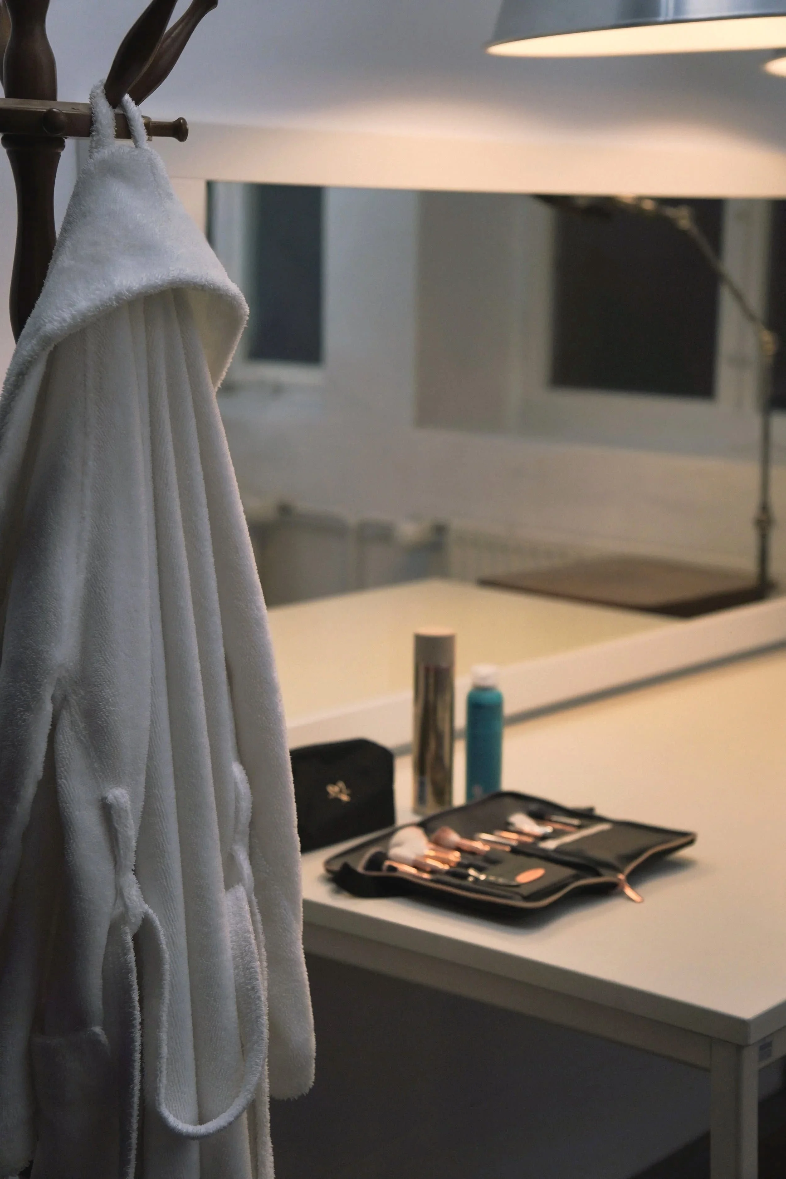 Eine Ankleide mit einem weißen Bademantel und Kosmetik-Tools auf einem Tisch, im Hintergrund ein Spiegel und ein Fenster.