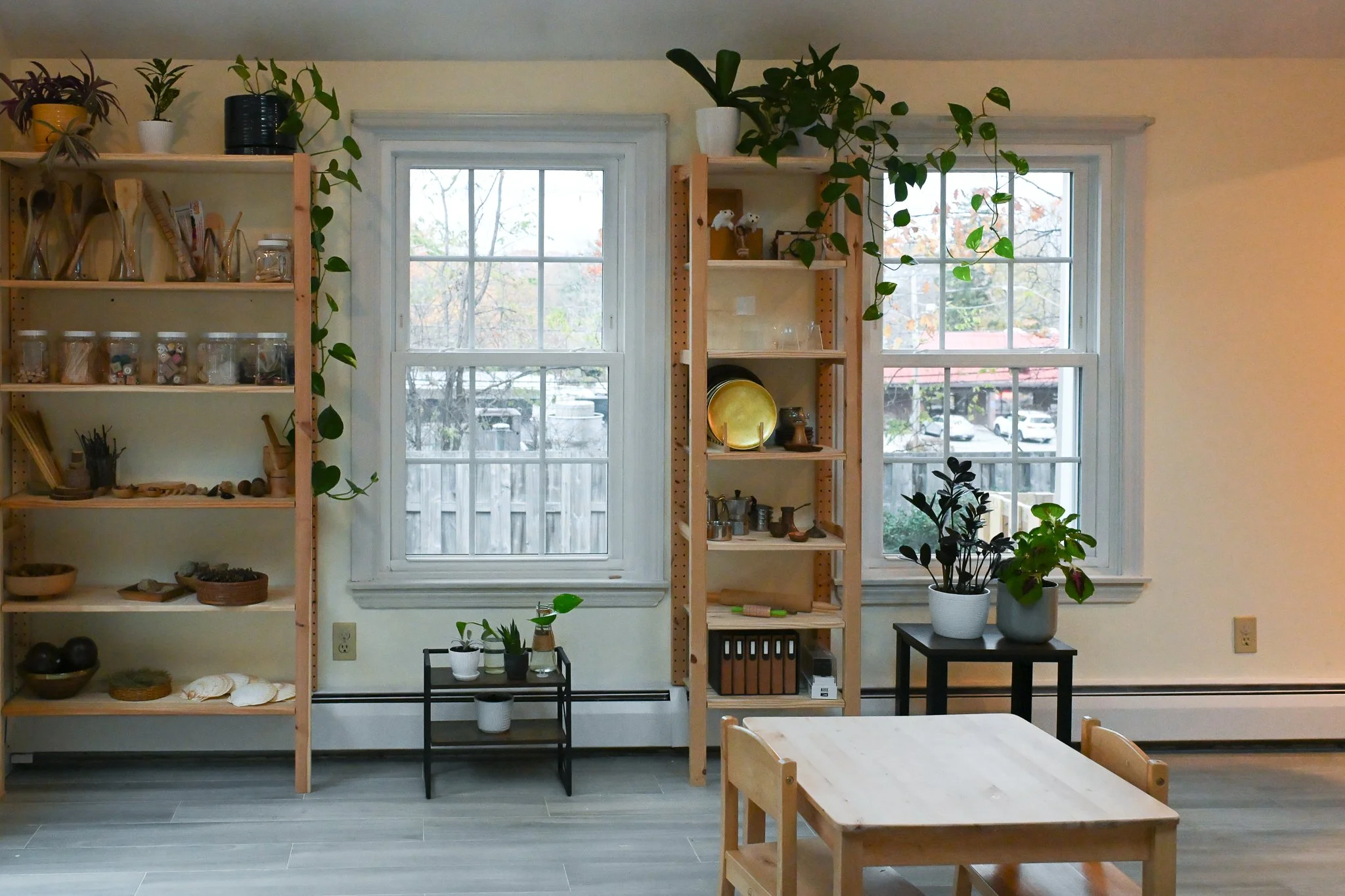 Room with two wooden shelves and clearly organized materials for play and exploration. The room organization offers teachers and children a sense of calm and comfort. Open shelves demonstrate a broad variety natural materials and live potted plants.