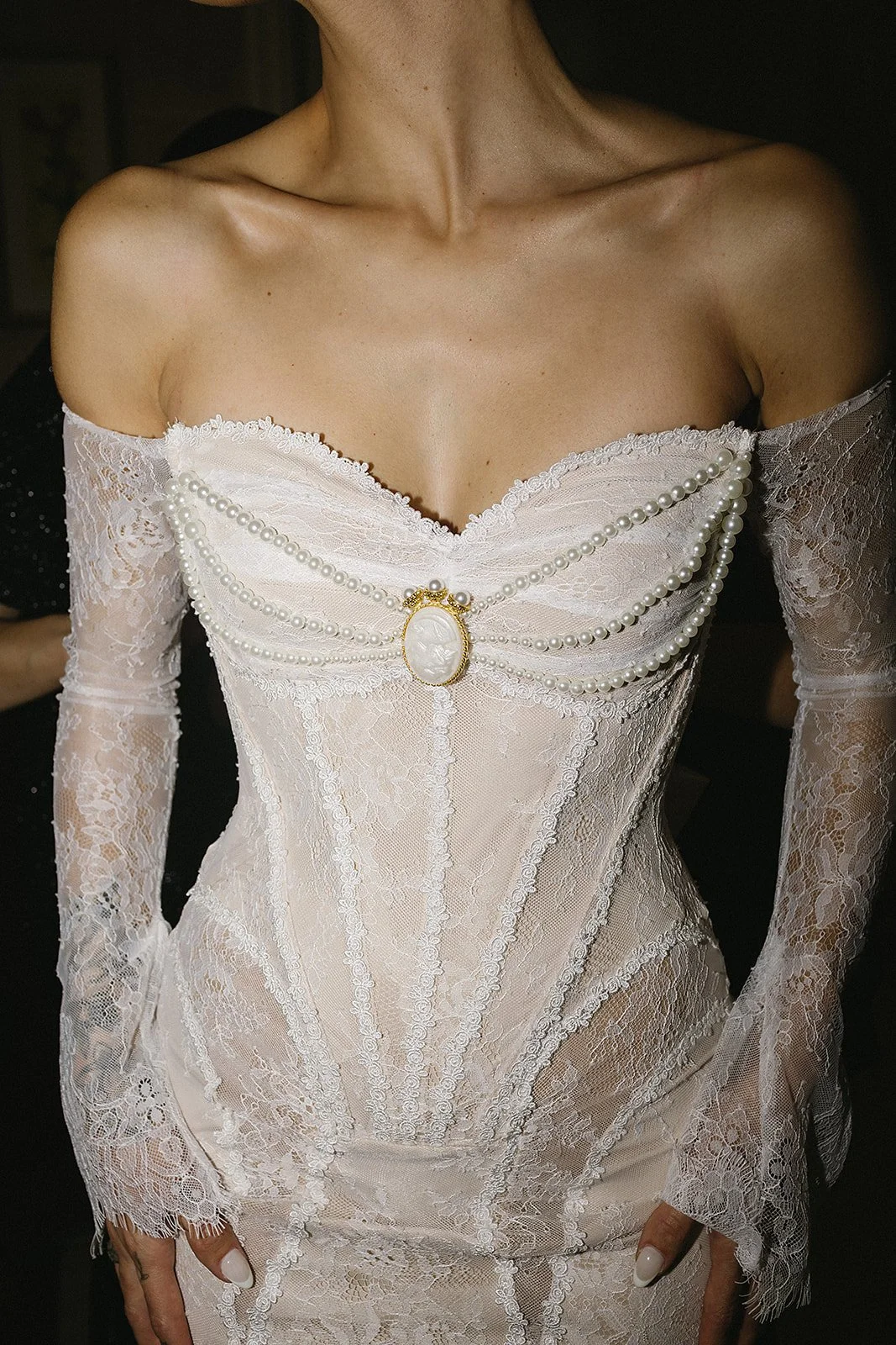 A woman wearing a vintage style off-shoulder lace dress adorned with pearl jewelry and an ornate cameo brooch.