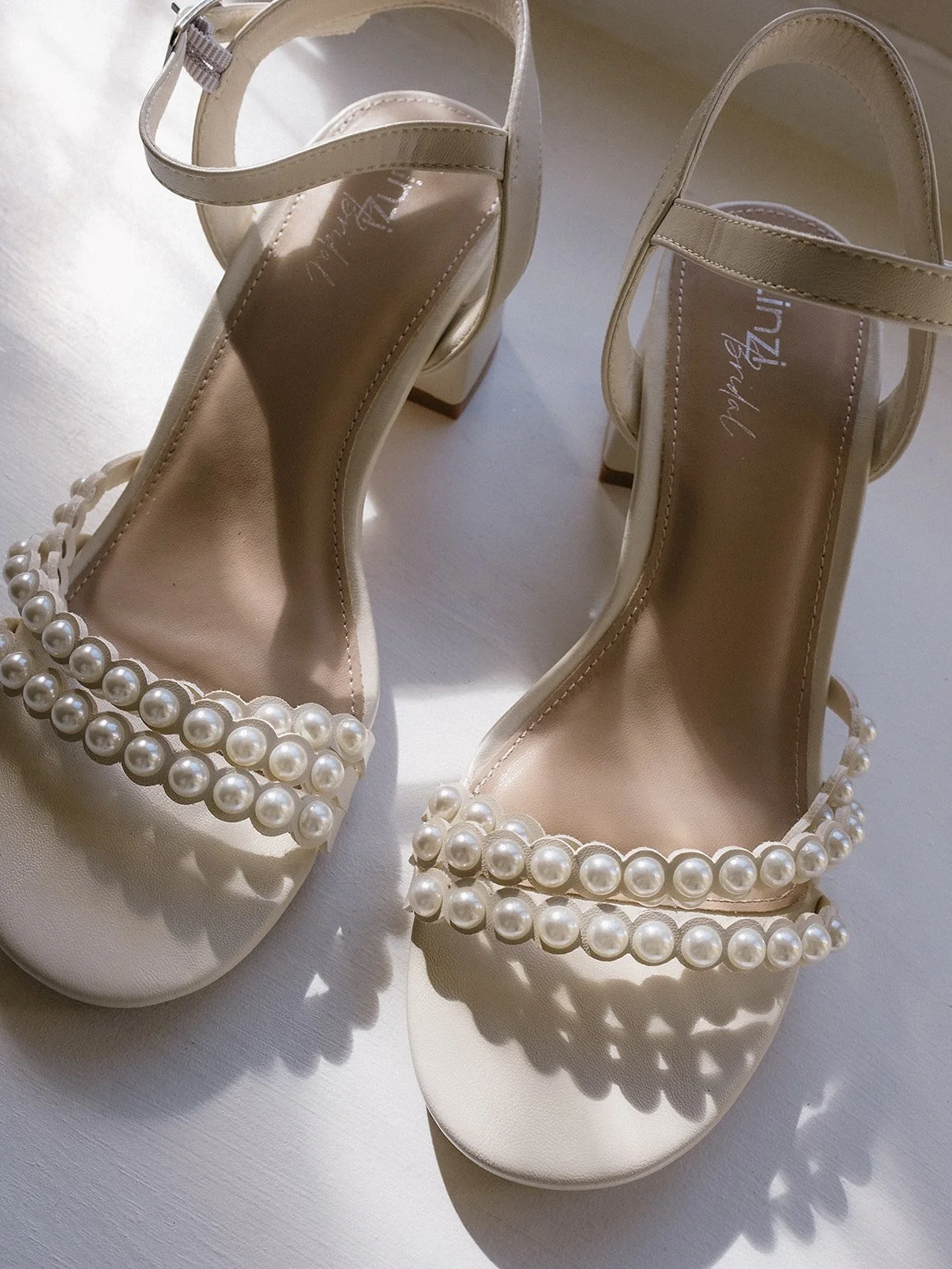 Close-up of a pair of elegant ivory high-heeled shoes decorated with large faux pearls on the straps at the toes.