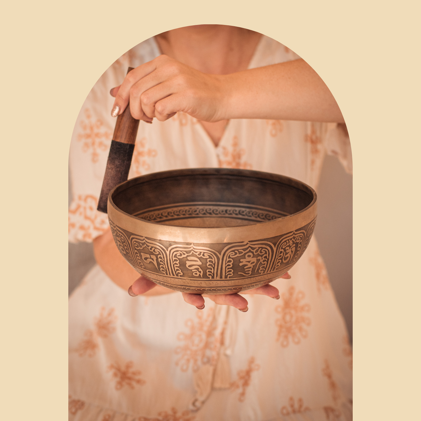 Jackie holding a Tibetan singing bowl in one hand and a wooden striker in the other, with a beige background.