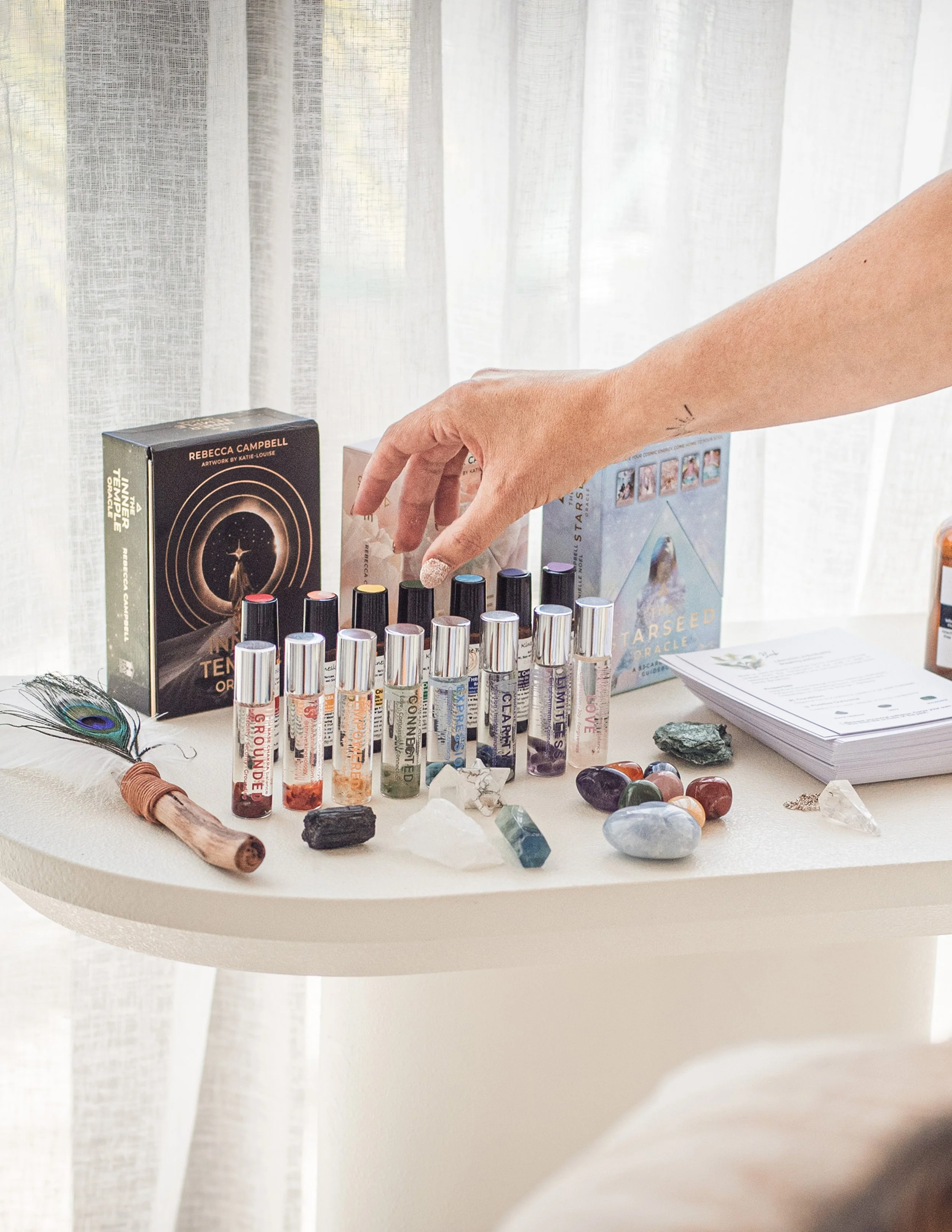 Some remedies we use in kinesiology. The table has wellbeing balancing oils, as well as various crystals, feather smudger, and some oracle card decks in the background.