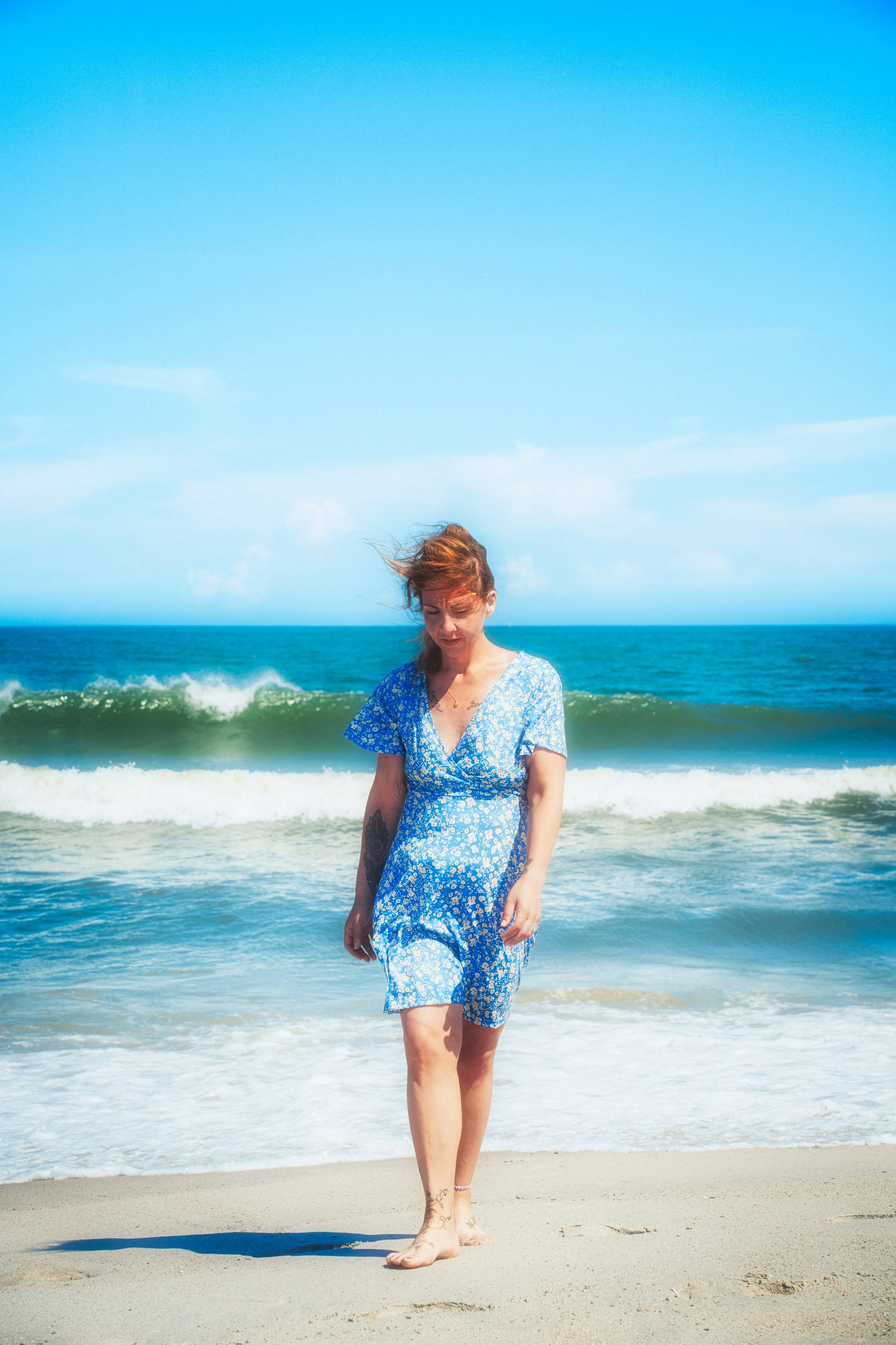A candid portrait captured along the shoreline as ocean waves roll in behind the subject under clear coastal light.