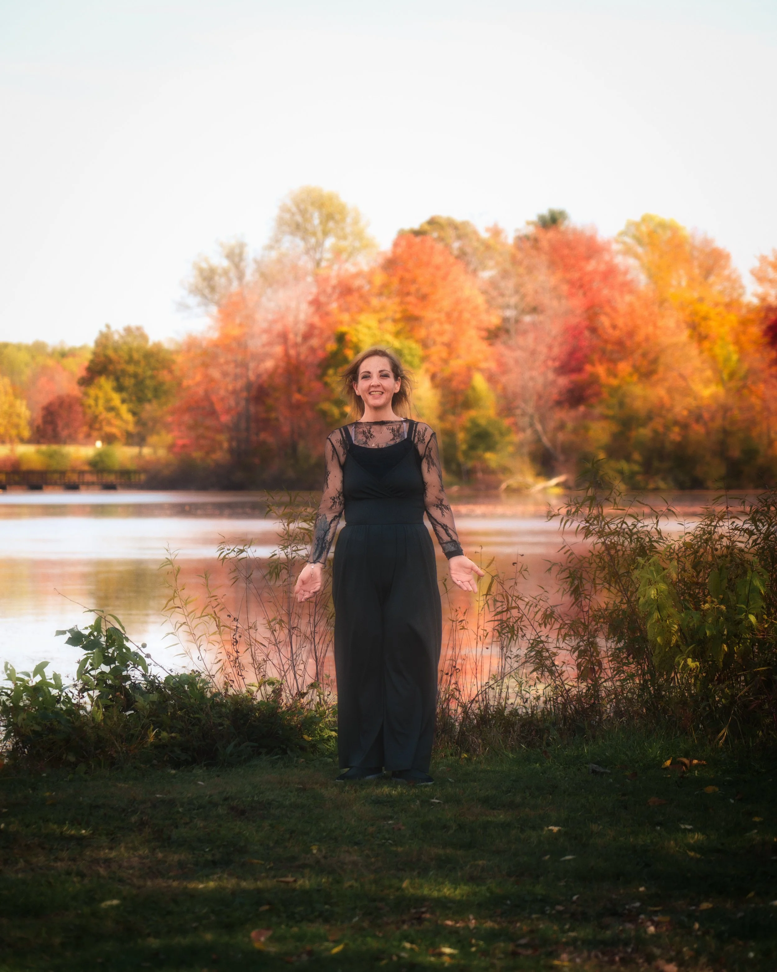 The subject stands against vibrant autumn foliage, blending portraiture with seasonal landscape elements.