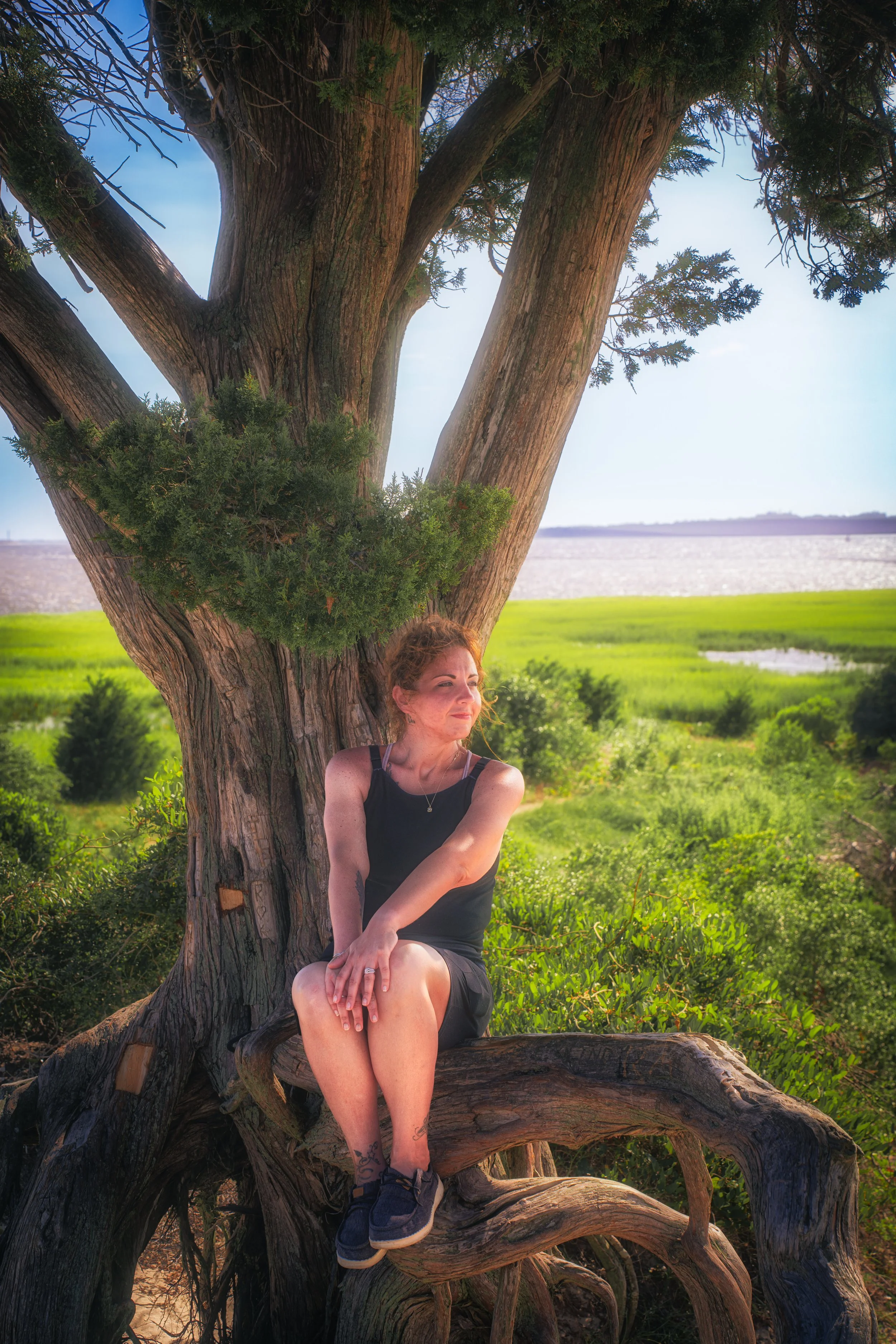 A relaxed portrait framed by trees and greenery, emphasizing connection between subject and environment.