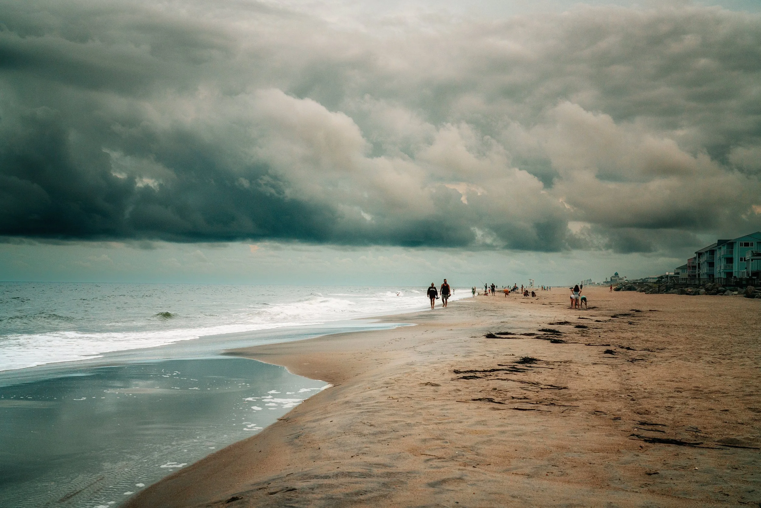 Dark storm clouds gathering over a wide shoreline and ocean surf.