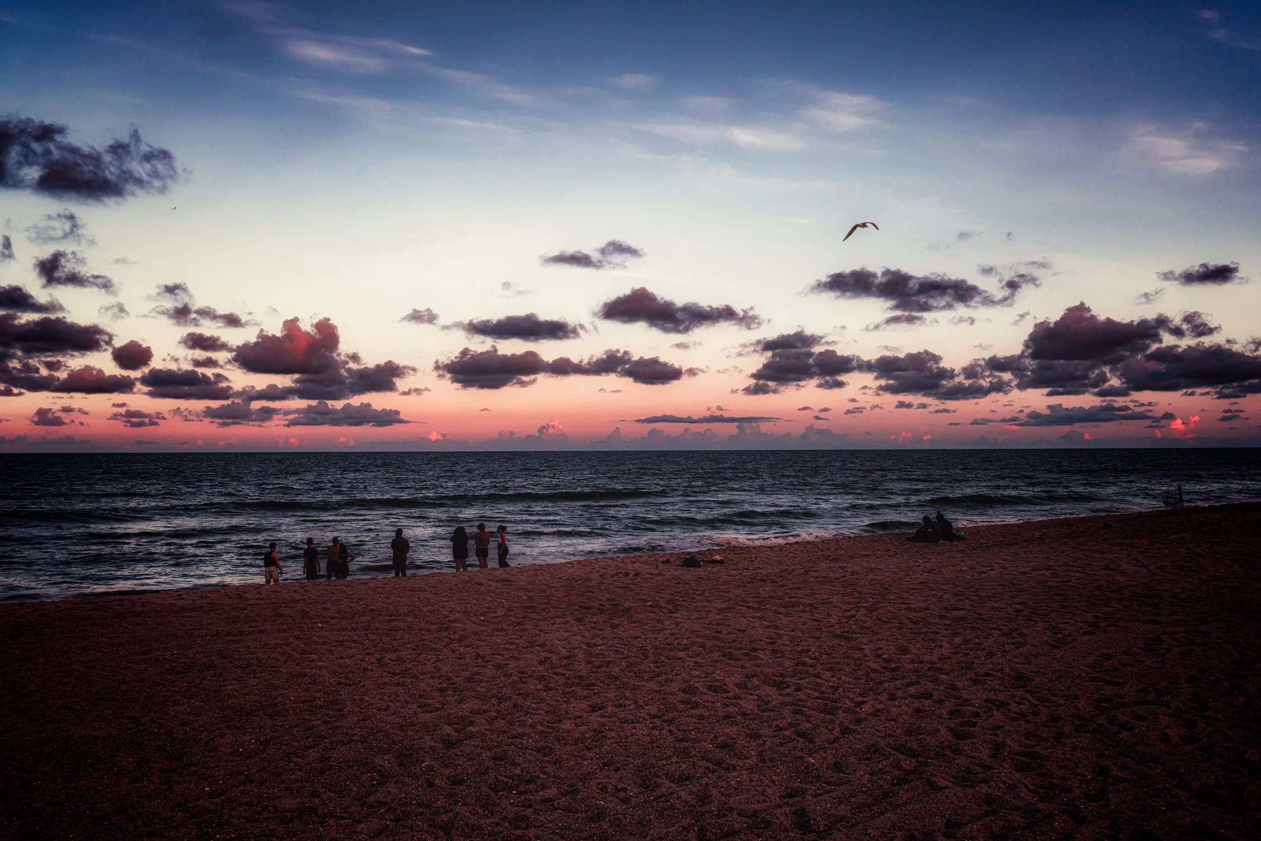 Visitors gather along the beach at sunset in Fort Fisher, North Carolina, as warm evening light fades over the Atlantic shoreline.