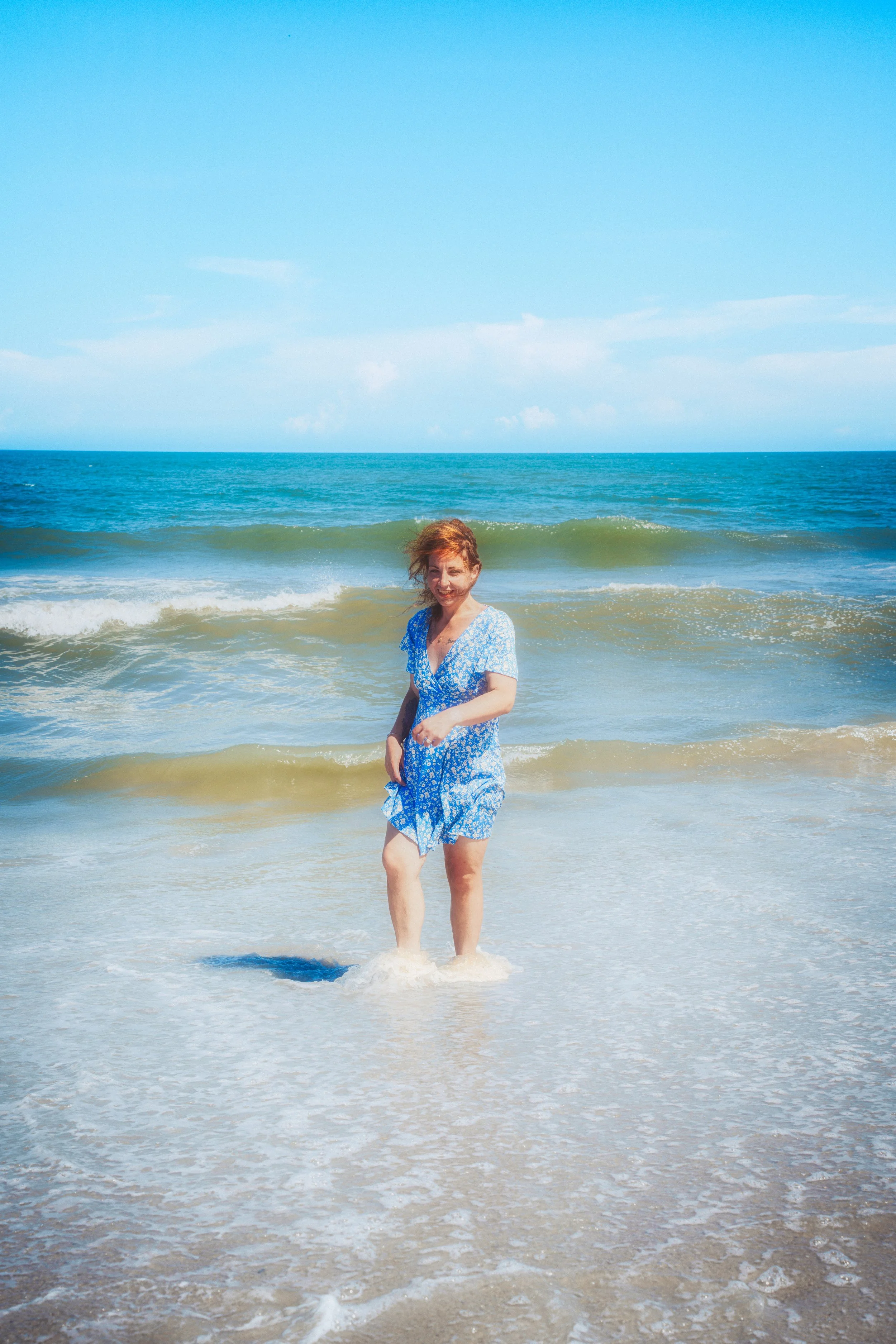 The subject pauses at the water’s edge as sunlight reflects off the ocean, capturing a spontaneous seaside portrait.