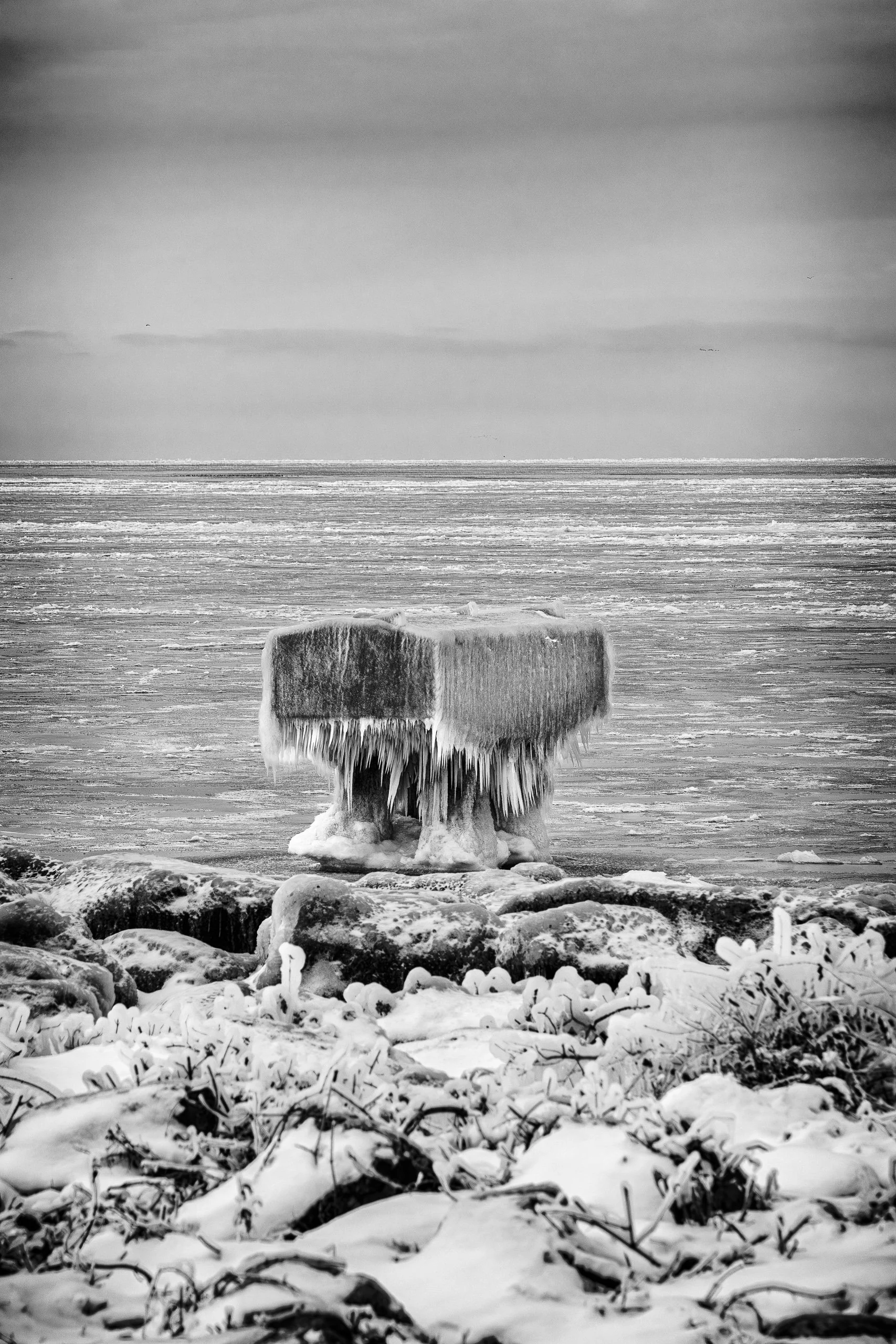 Ice gathers around a lakeside structure, transforming familiar shapes into abstract winter textures.