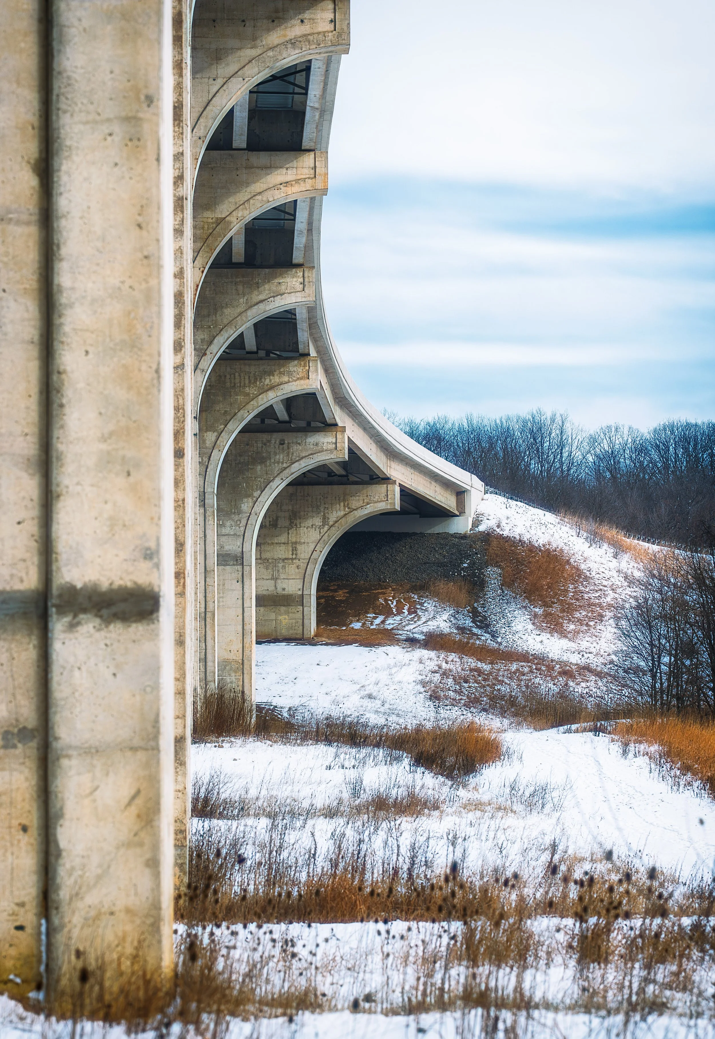 An arched bridge extends across a snow-covered scene, highlighting the contrast between architecture and seasonal stillness.