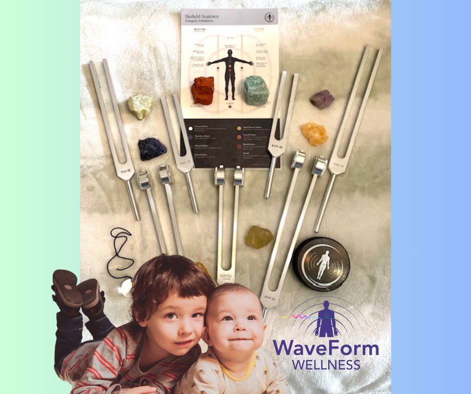 A tabletop display of jewelry tools, gemstones, and an anatomy chart, with two children lying in front and a logo for WaveForm Wellness.