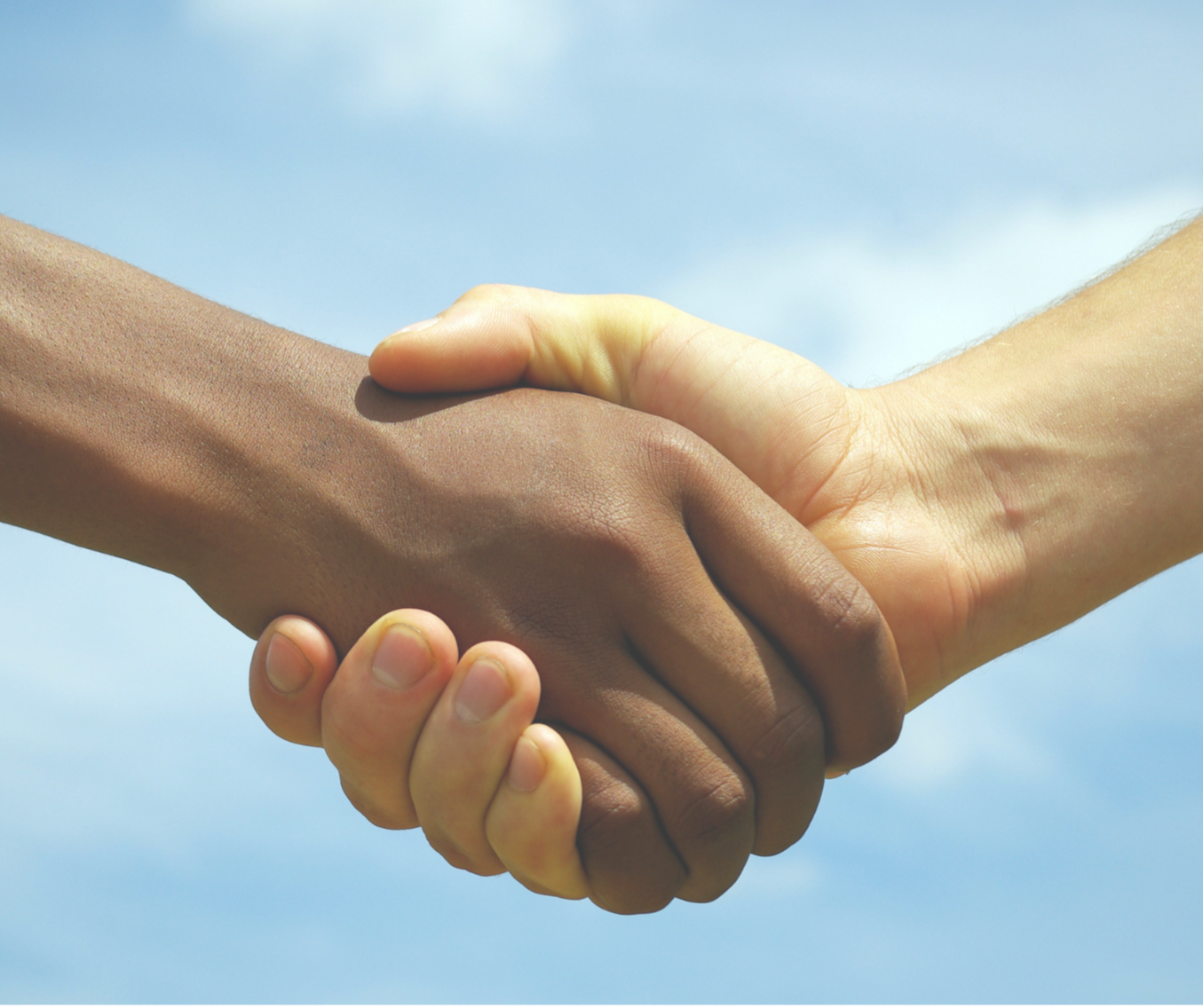 Close-up of two people shaking hands, one with dark skin and the other with light skin, against a cloudy sky background.