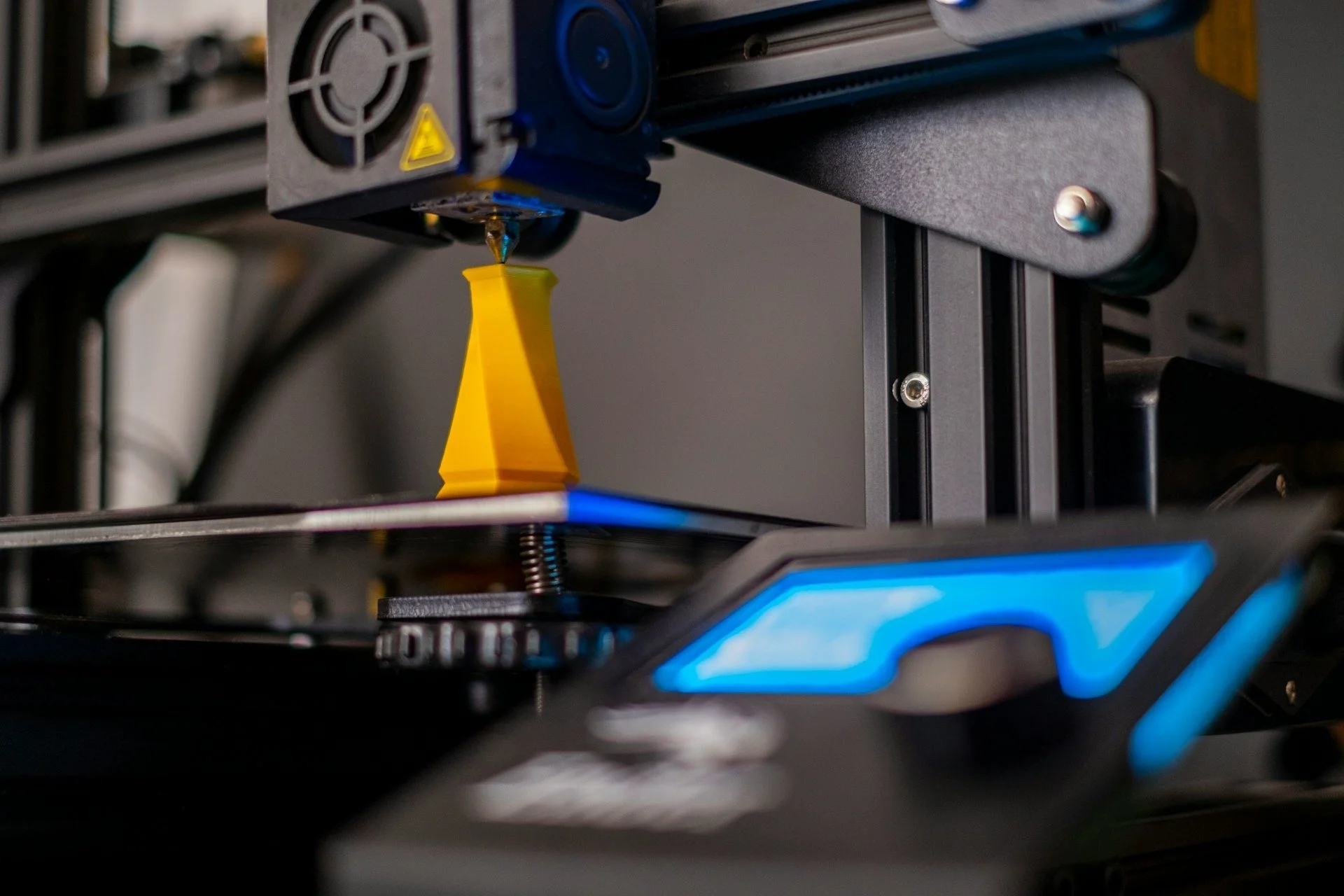 Close-up of a 3D printer in action, with a yellow 3D-printed object being created on the print bed.