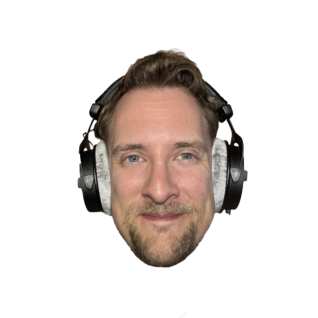 A man with light brown hair, a beard, and blue eyes wearing large over-ear headphones, smiling at the camera.