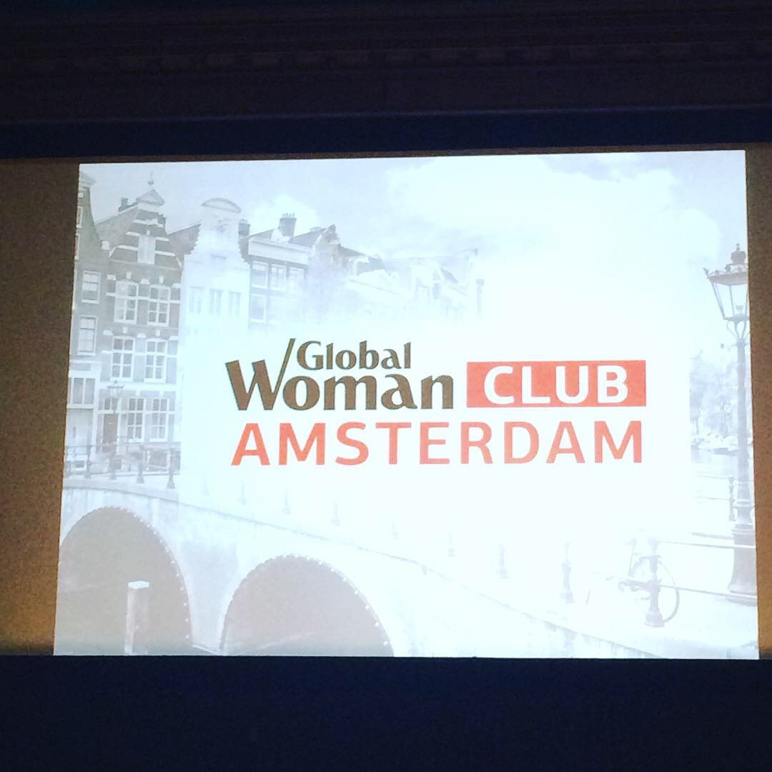Slide showing the logo of Global Woman Club Amsterdam with a background of Amsterdam buildings and canal.