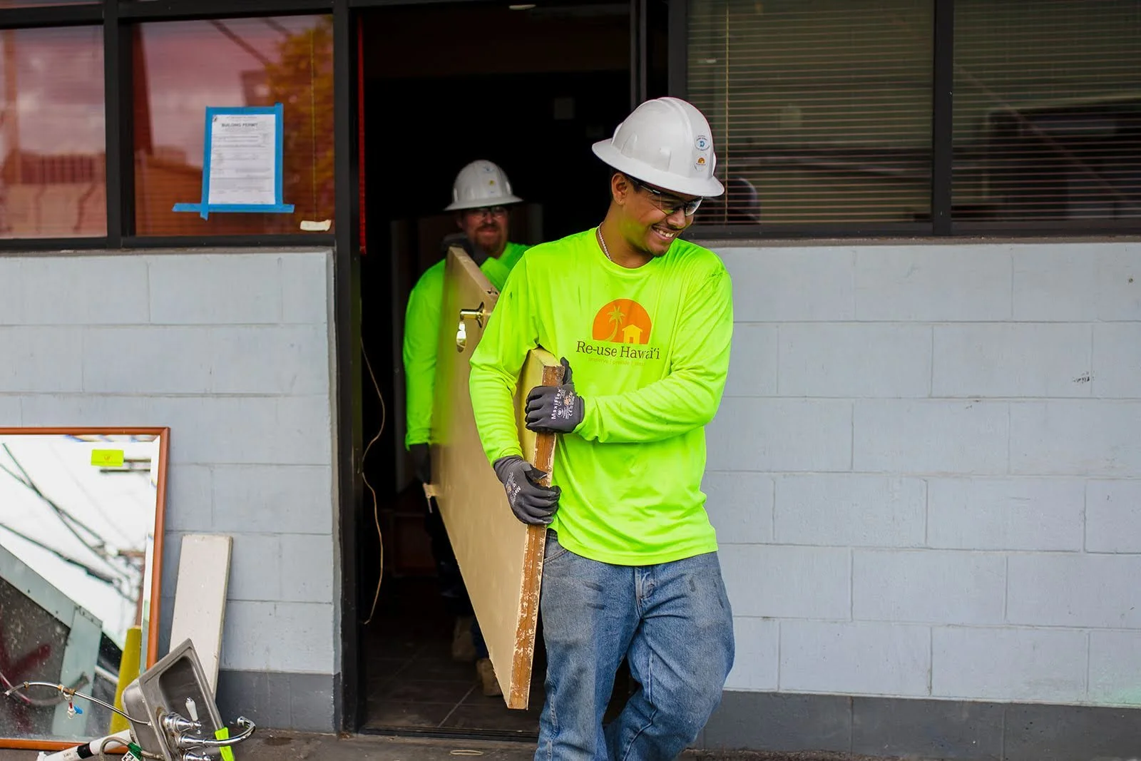 Two men working together to carry a door out of a commercial building. 