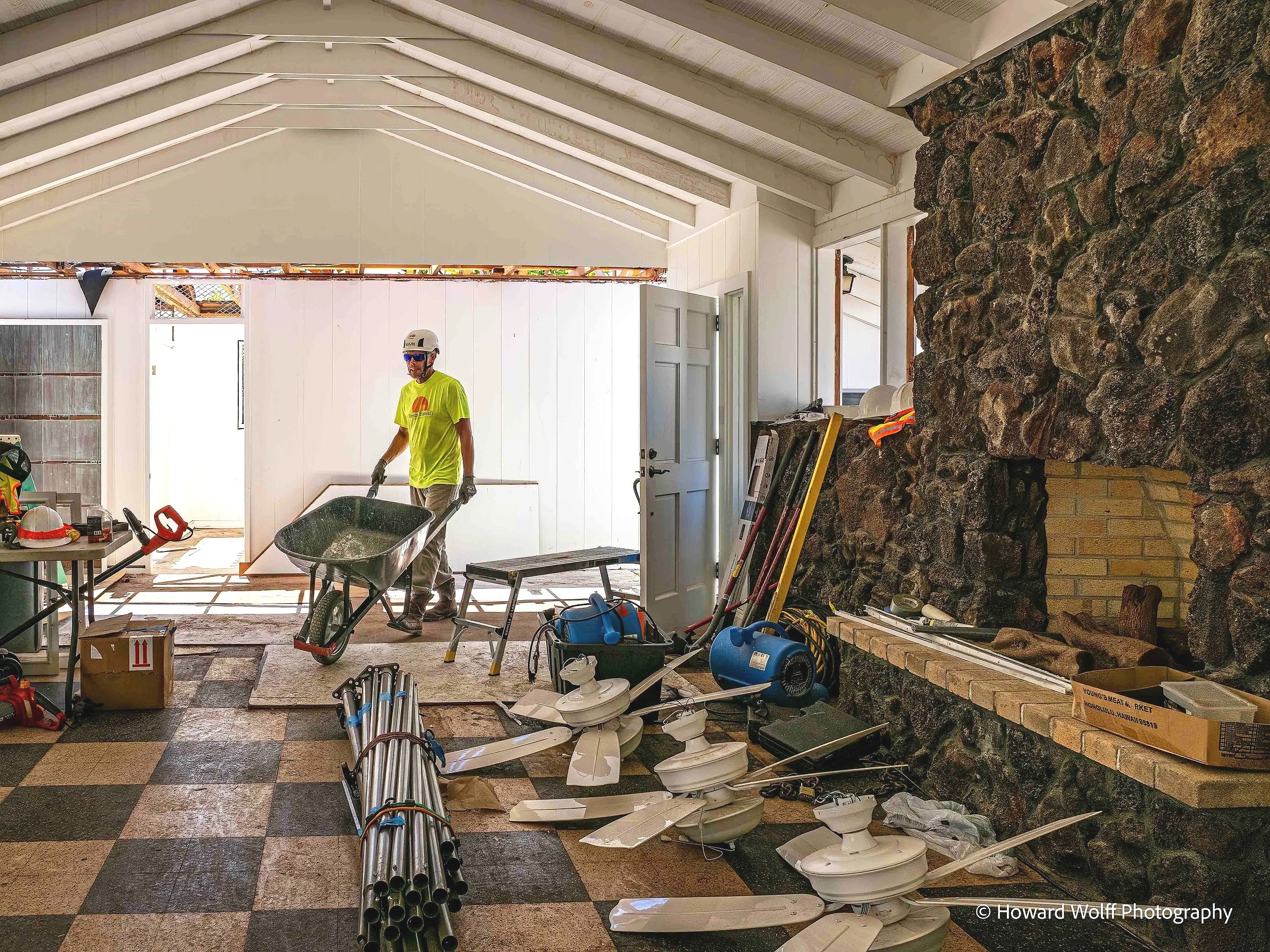 A deconstruction crew member using a wheel burrow to carry materials through a room under construction.