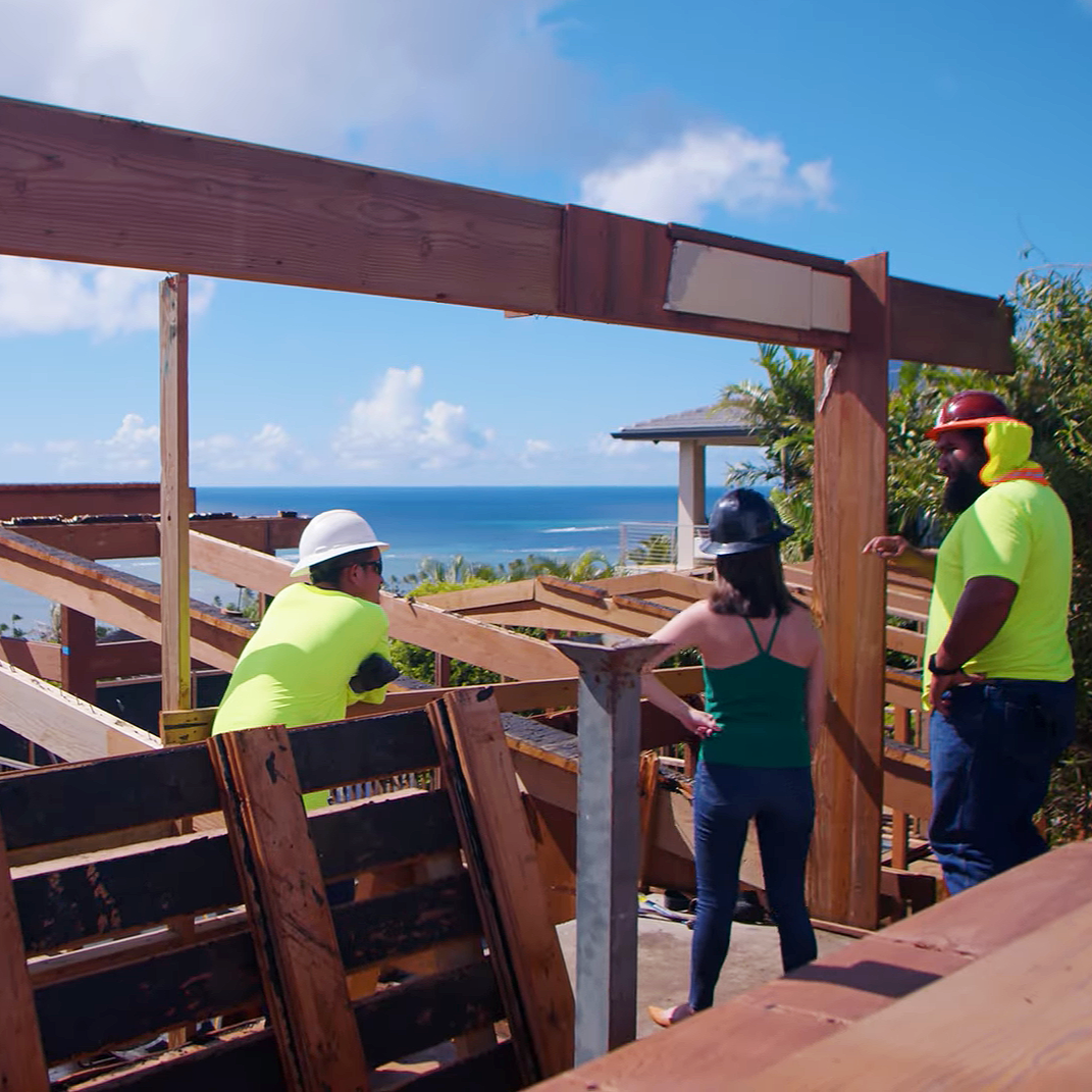 Two men and one woman stand at a home deconstruction site with an ocean view to discuss the project.