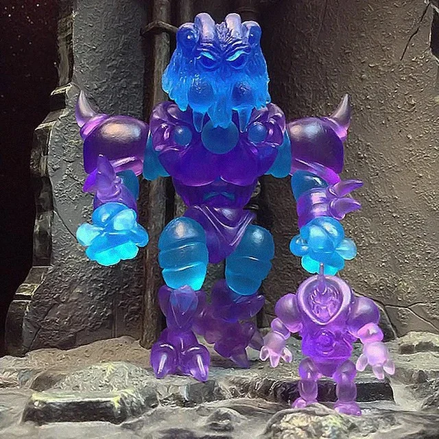 Colorful glow-in-the-dark dragon and humanoid figure statues standing on rocky ground against a textured stone wall.