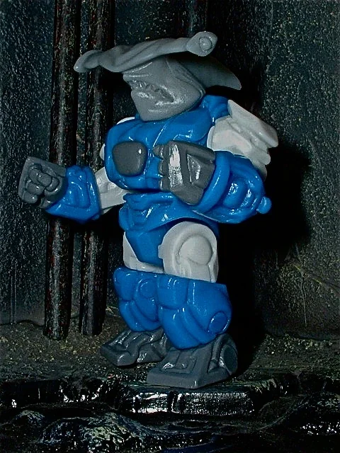 A figurine of a cartoon goblin character dressed as a ninja, in a blue and gray outfit, with a posed stance and a sword behind its back.