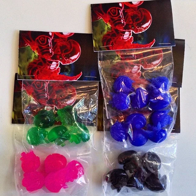 Four small packets of nail polish in pink, green, blue, and black, with dragon-themed images in the background.