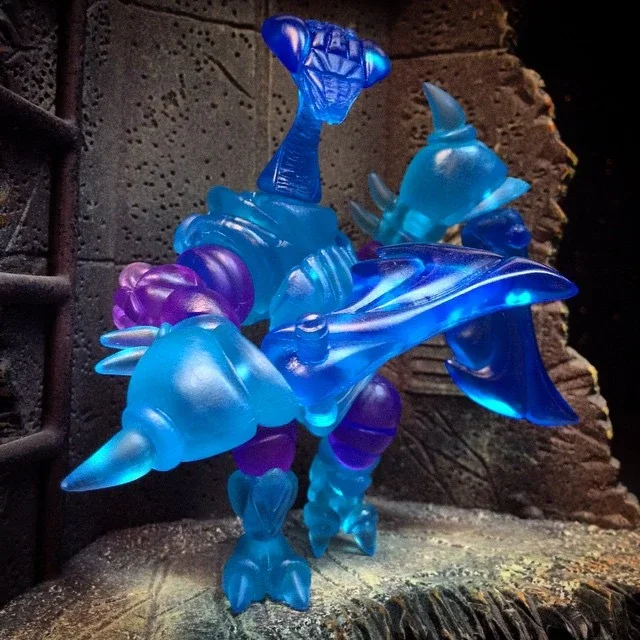 Colorful glass sculpture of a unicorn with a blue body, purple mane, and tail on a rustic wooden surface.