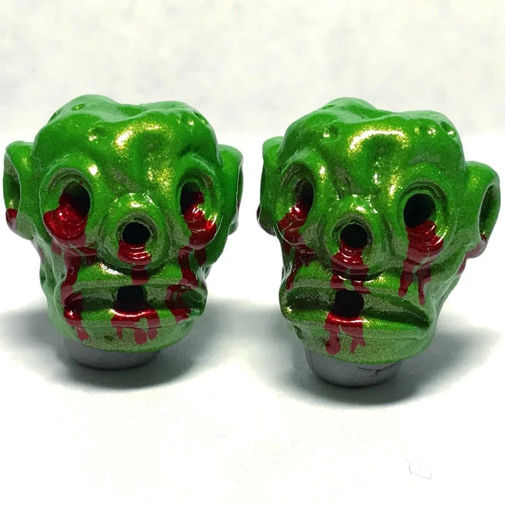 Green skull-shaped objects with red streaks, possibly resembling blood, on a white surface.