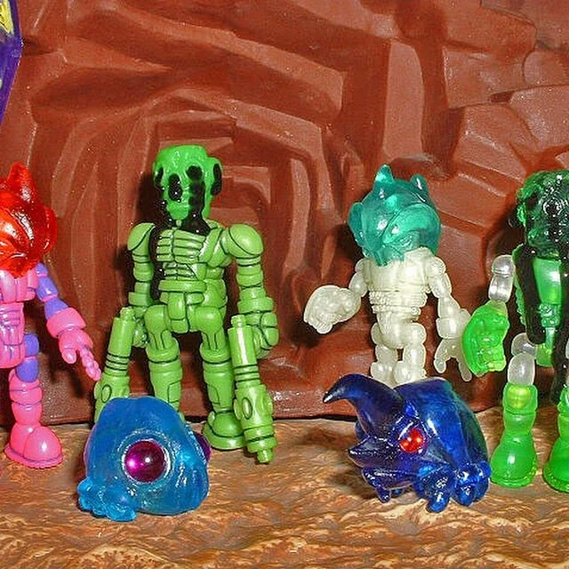 Collection of small, colorful plastic toy figurines, including fantasy characters and creatures, set against a textured brown background.