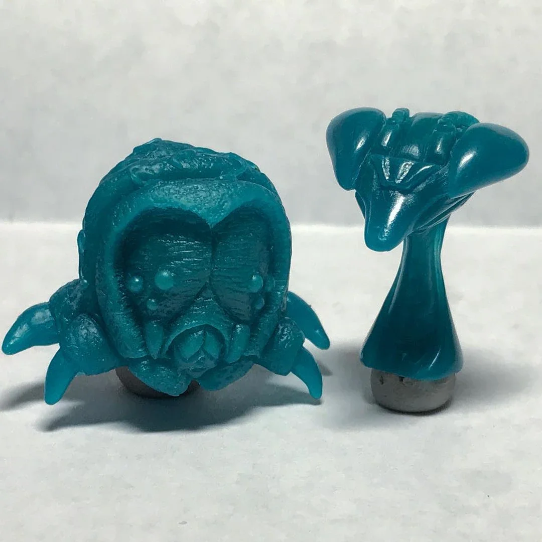 Two blue, intricately carved objects resembling a creature and an abstract figure, placed on a white surface against a plain gray background.