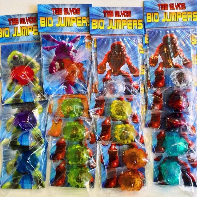 Five packages of toy bio jumpers with colorful monster figures in clear plastic bags, displayed on a blue background.