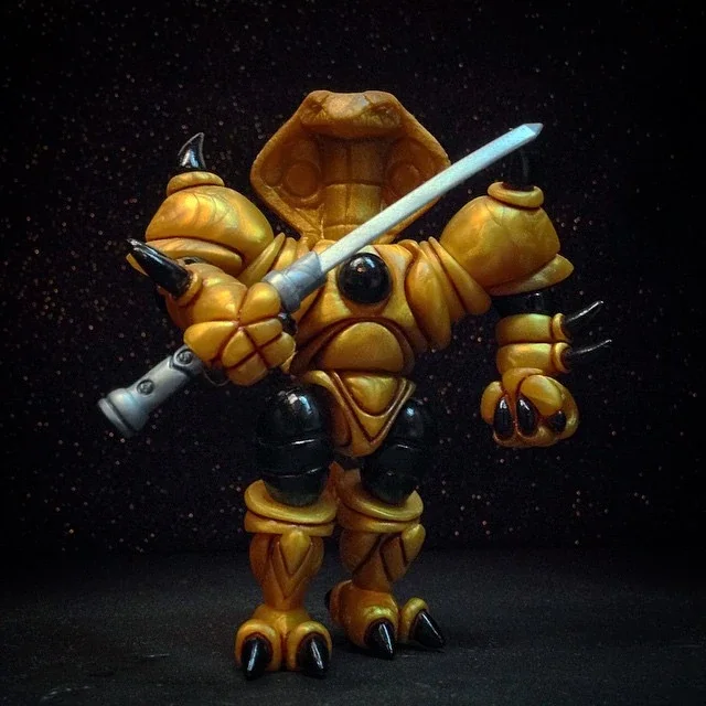 A detailed figurine of a robotic creature resembling a warrior with orange and black armor, holding a silver sword, set against a black background with specks of light.