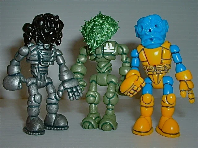 Three small, colorful robot action figures standing on a surface, each with distinct features and colors.