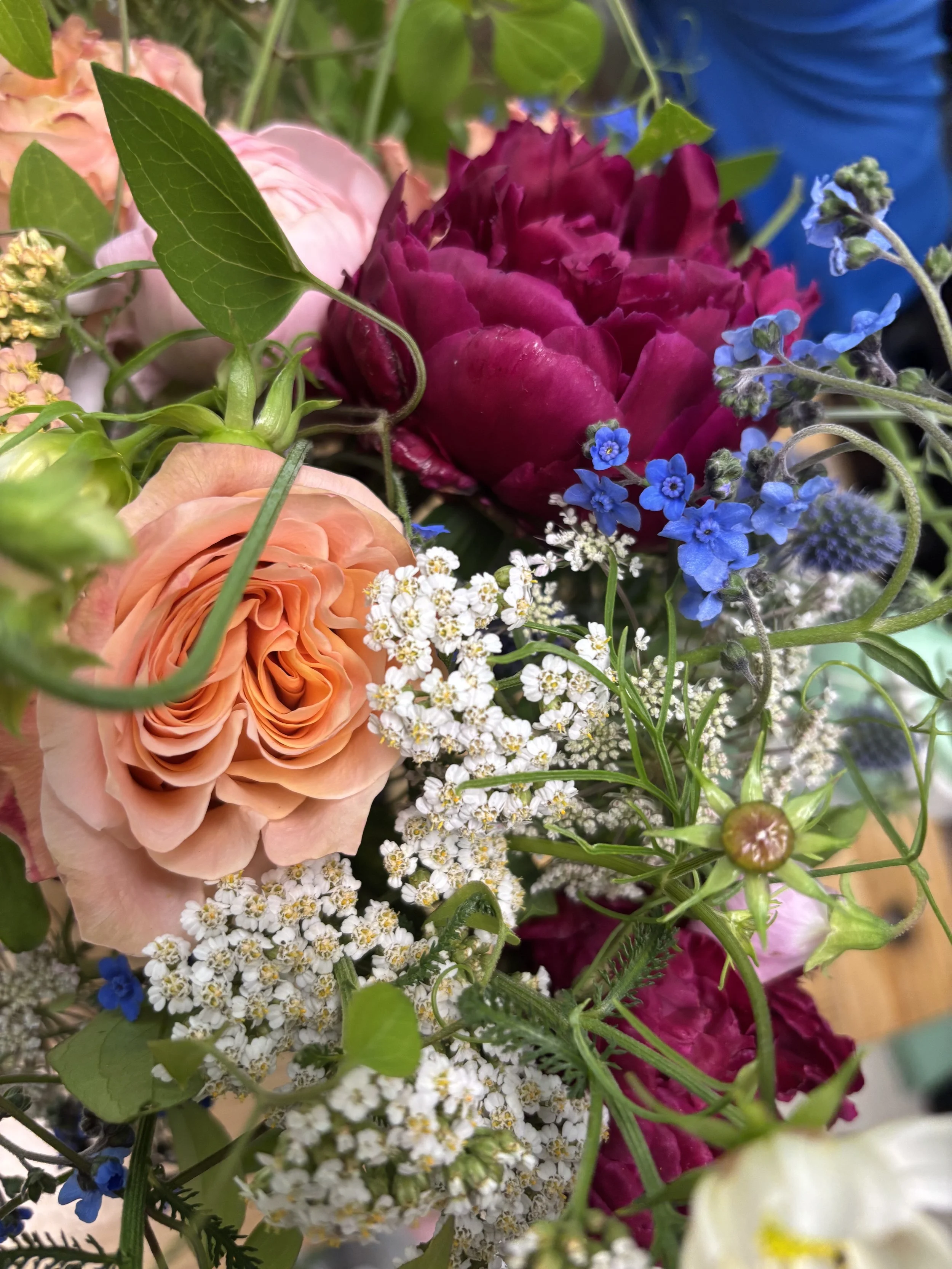 Close-up of a colorful flower bouquet with pink, purple, blue, and white flowers and green leaves.