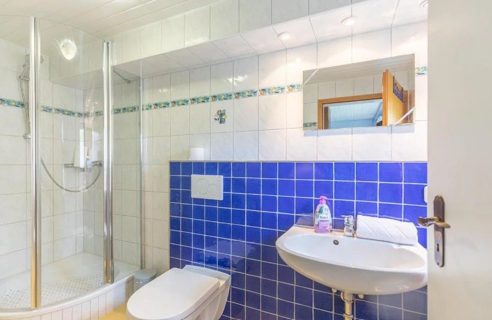 Kleines Badezimmer mit Dusche, Toilette und Waschbecken, blauer und weißer Fliesenwand, Spiegel und Handtuch auf dem Waschbecken