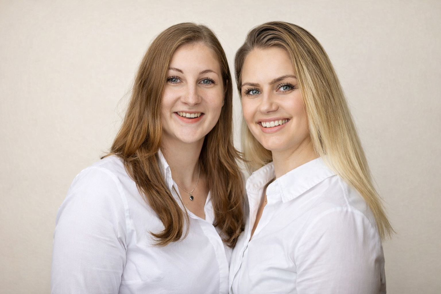 Die beiden lächelnden Geschäftsführerinnen von L&P Living im weißen Hemden vor heller Wand.