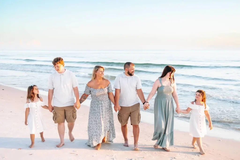 Family walking hand in hand along the beach at sunset, with ocean waves in the background.
