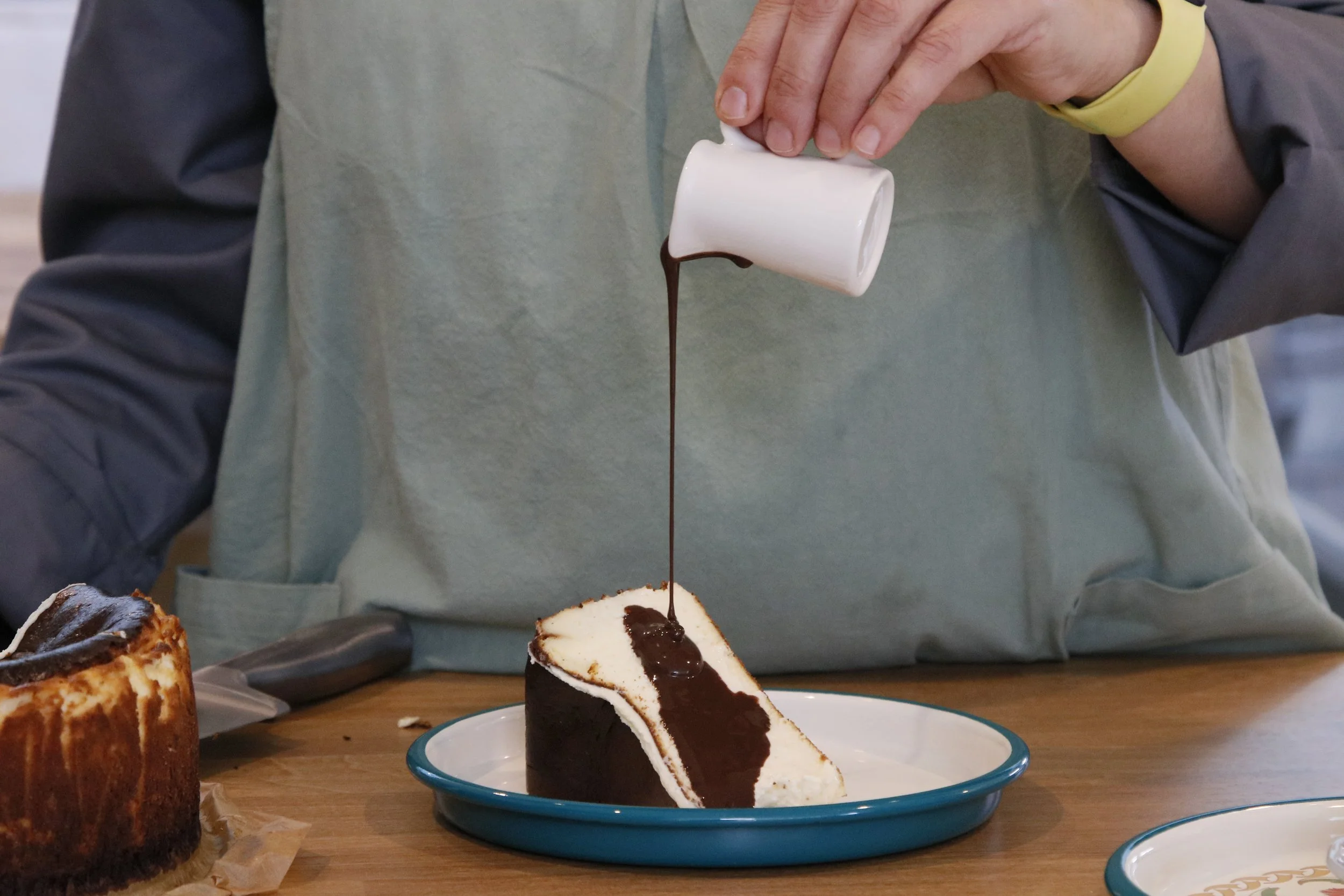 Berna’s Bakery San Sebastián cheesecake topped with warm, rich chocolate sauce, freshly poured for dessert lovers in Issaquah.