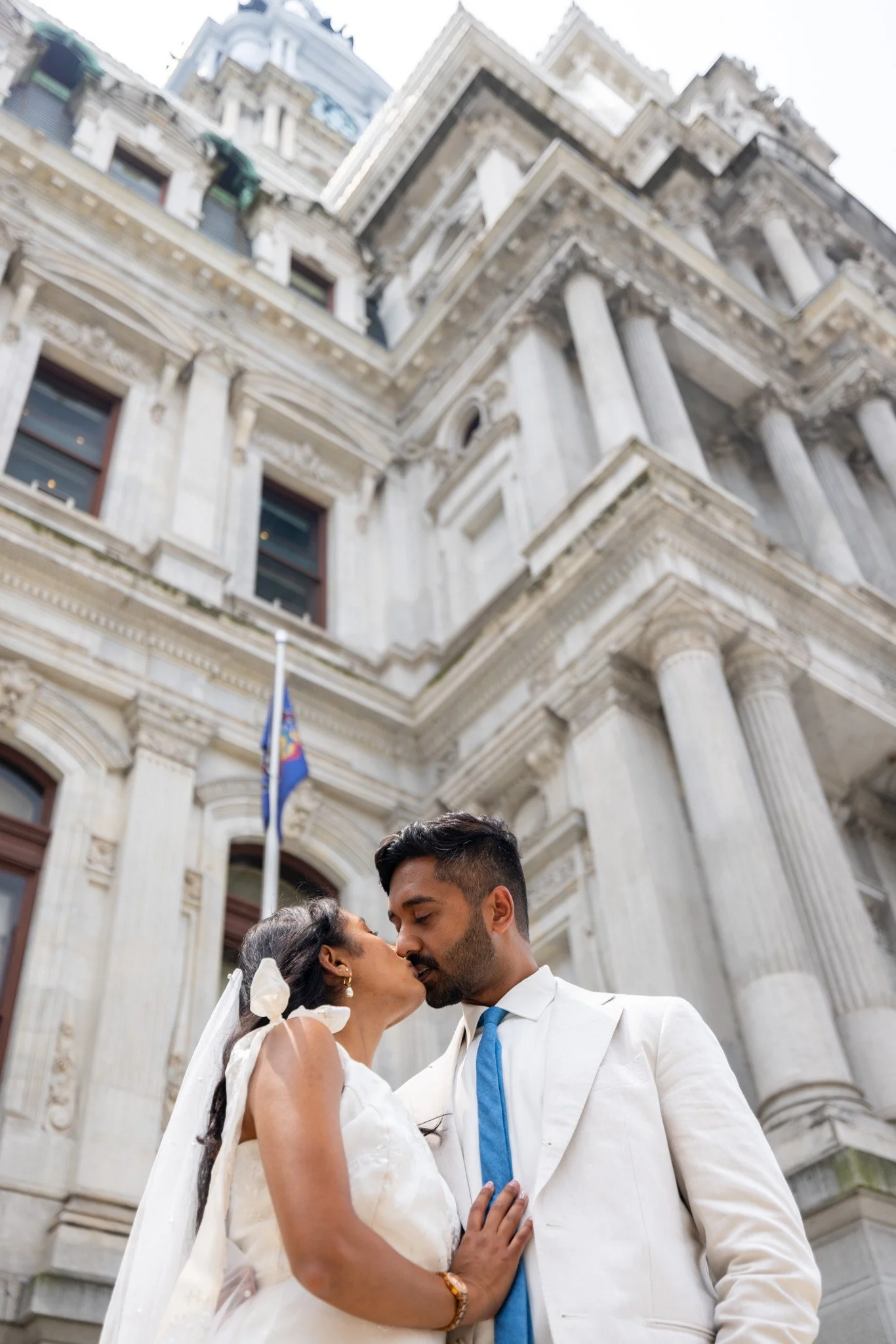 Engaged couple kissing in front of Philadelphia City Hall during an engagement photo session by David Pierre Studio