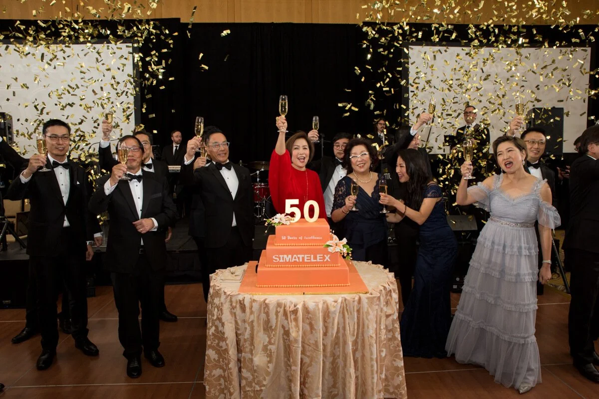 Guests toasting as confetti falls around a 50th anniversary cake at a corporate gala, event photography by David Pierre Studio
