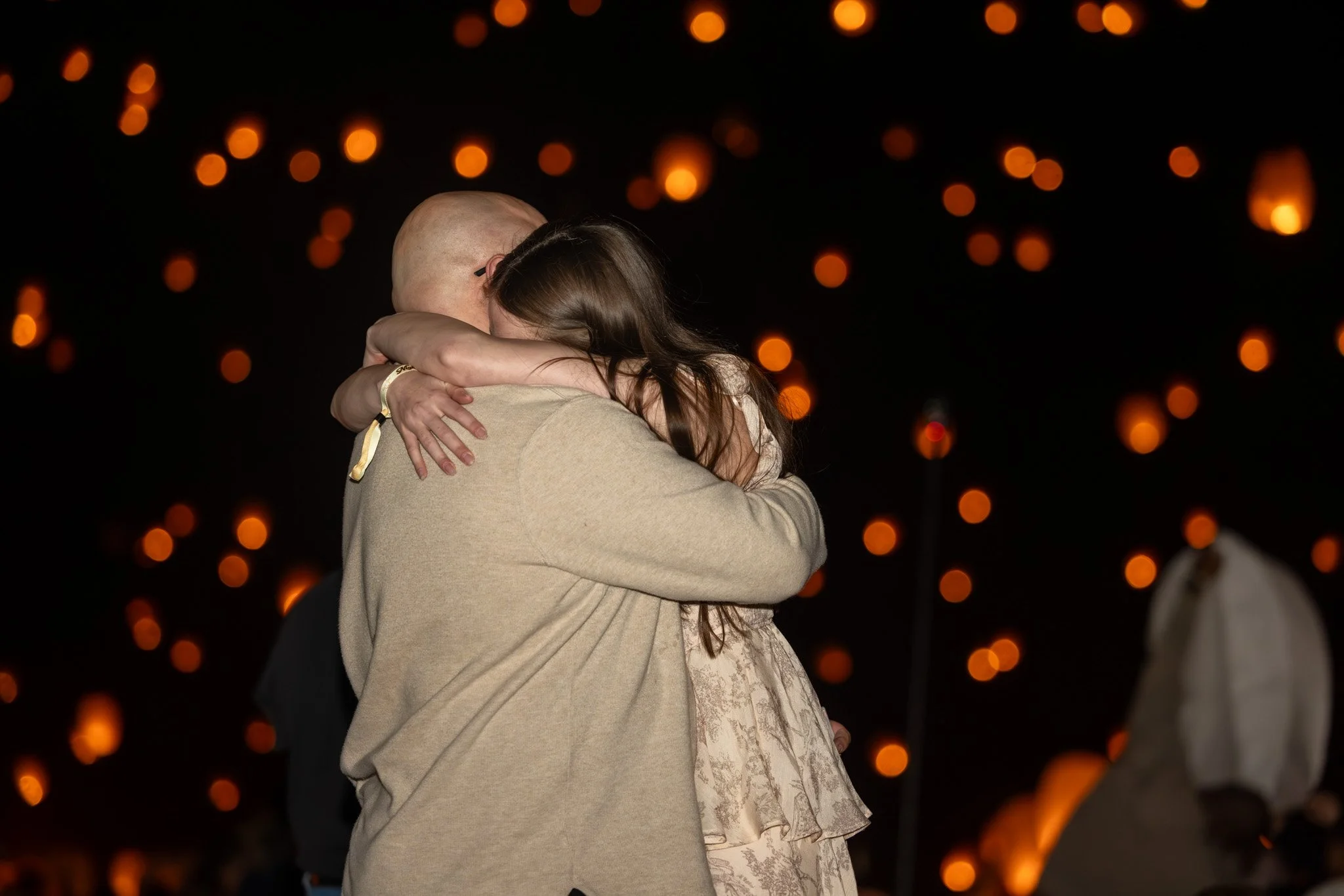 Couple embracing under glowing floating lanterns at night during an engagement session at Pocono Raceway