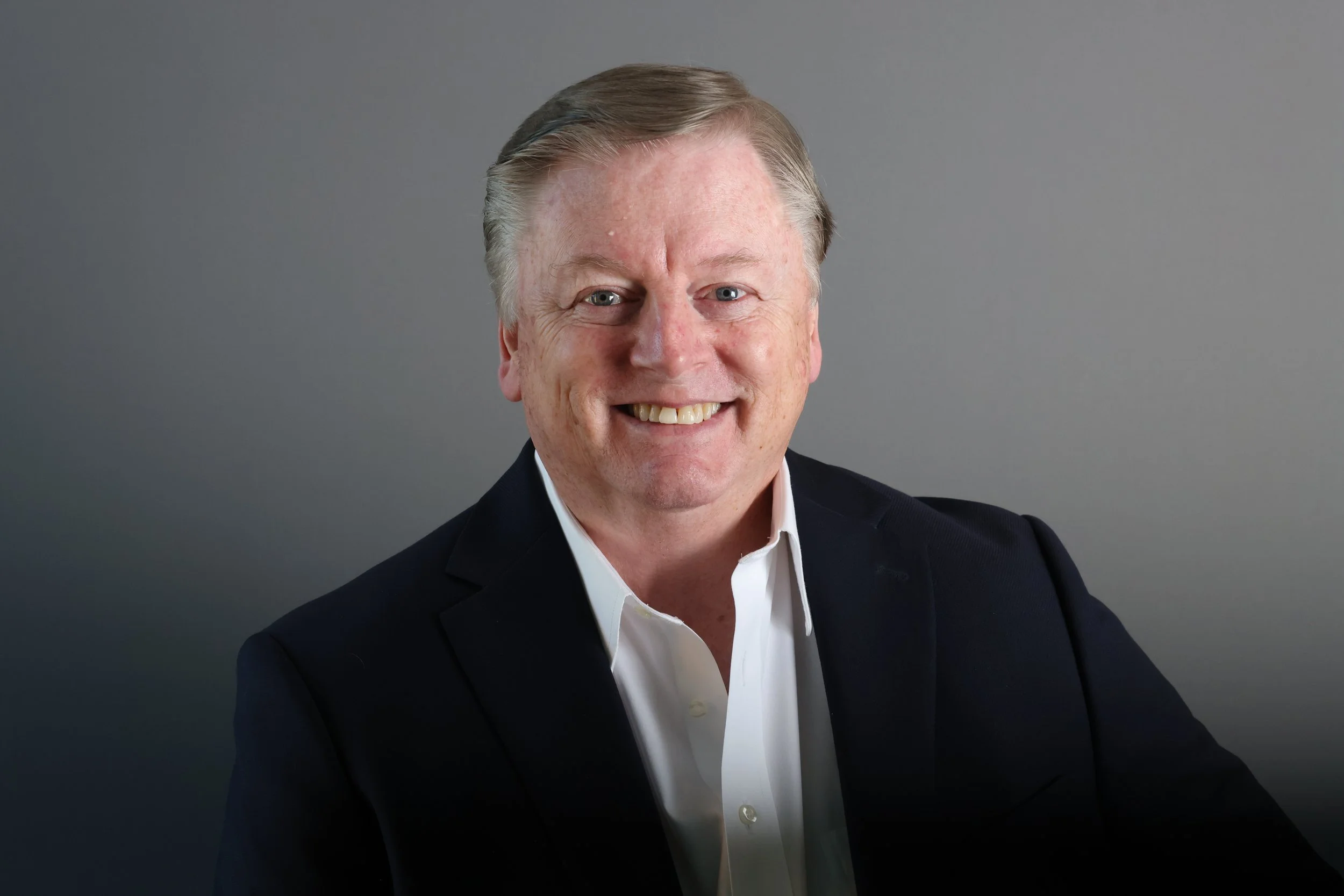 Professional corporate headshot of a smiling executive in a dark suit, headshot photography by David Pierre Studio