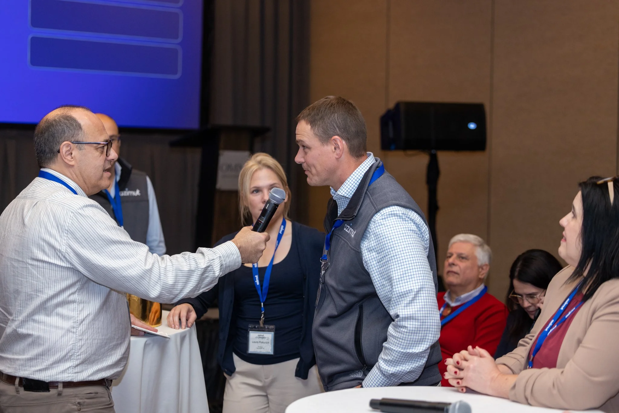 Attendee asking a question into a handheld microphone during a corporate conference Q&A session, captured by David Pierre Studio