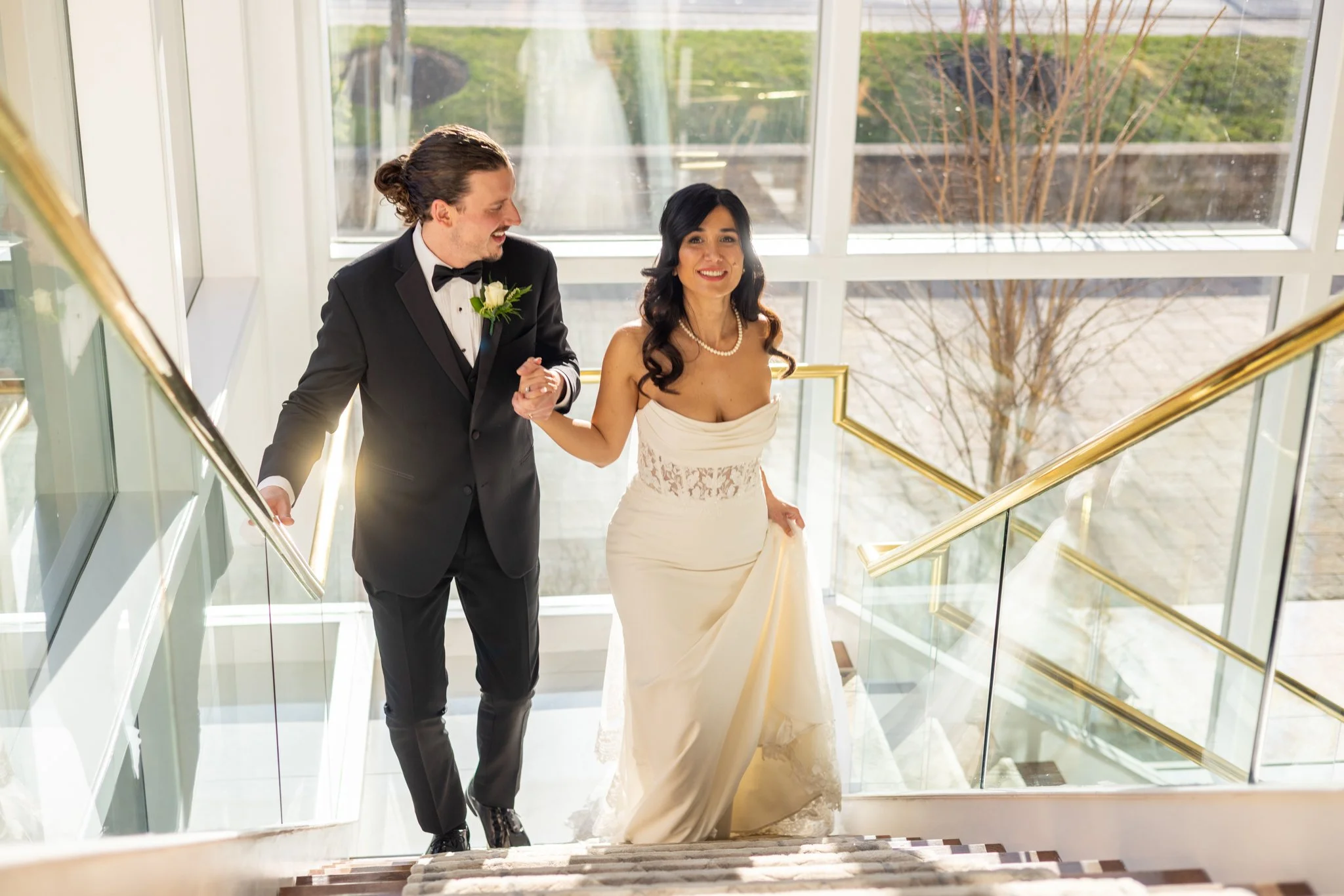 Bride and groom walking up a glass staircase on their wedding day, wedding photography by David Pierre Studio