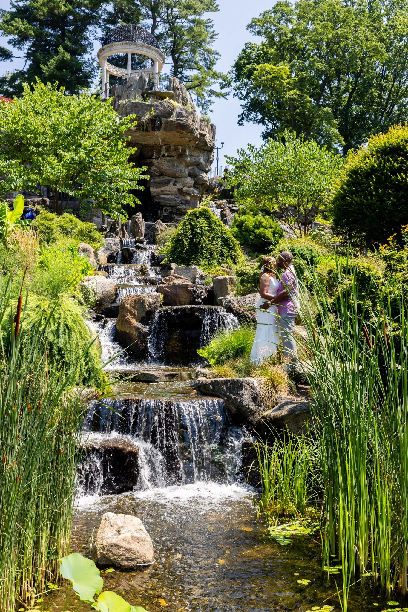 Couple embracing beside the waterfall and rock temple gazebo at Untermyer Gardens Conservancy in Yonkers, New York