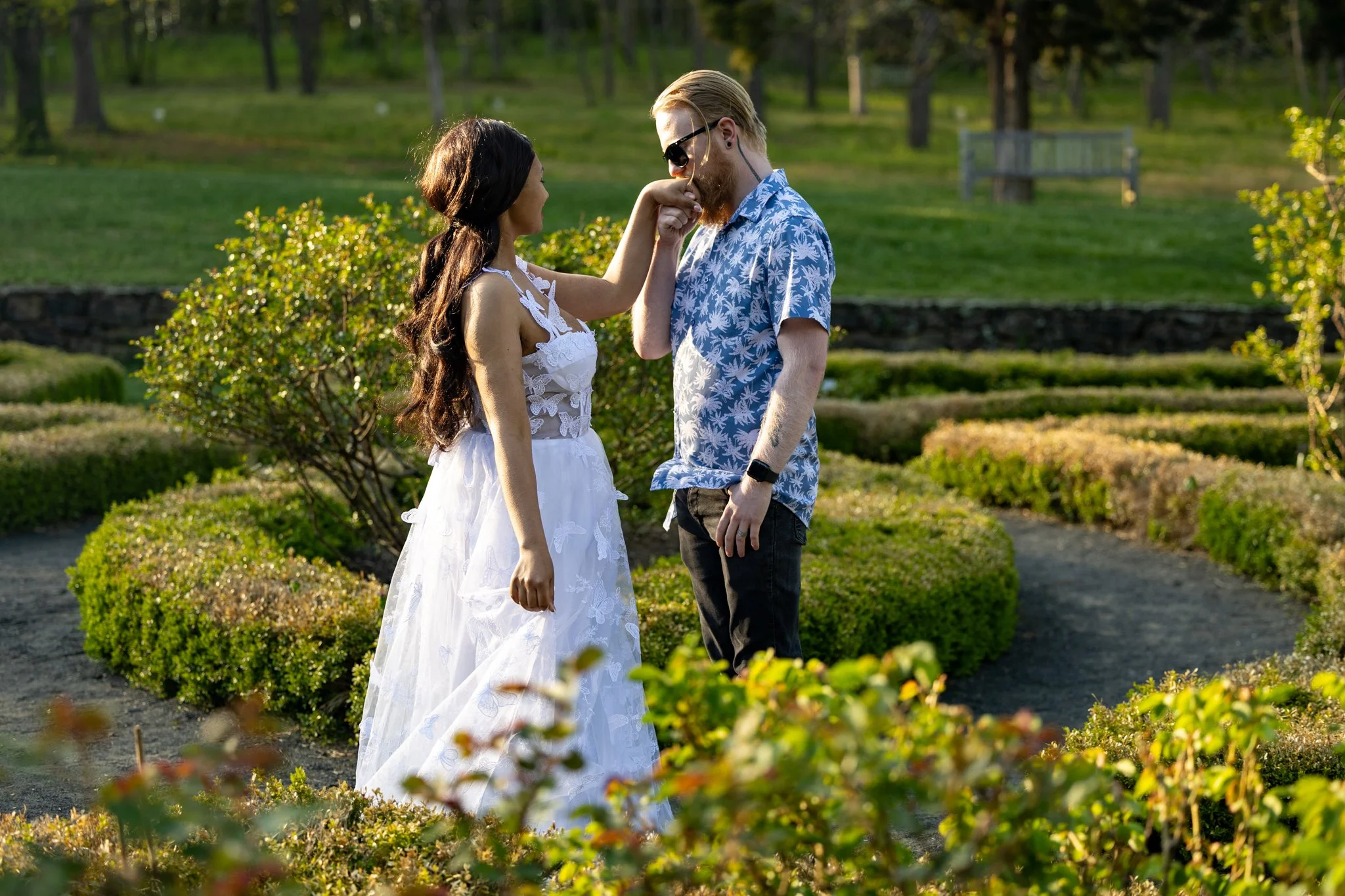 Man kissing his fiancee's hand in a manicured garden, engagement photography by David Pierre Studio