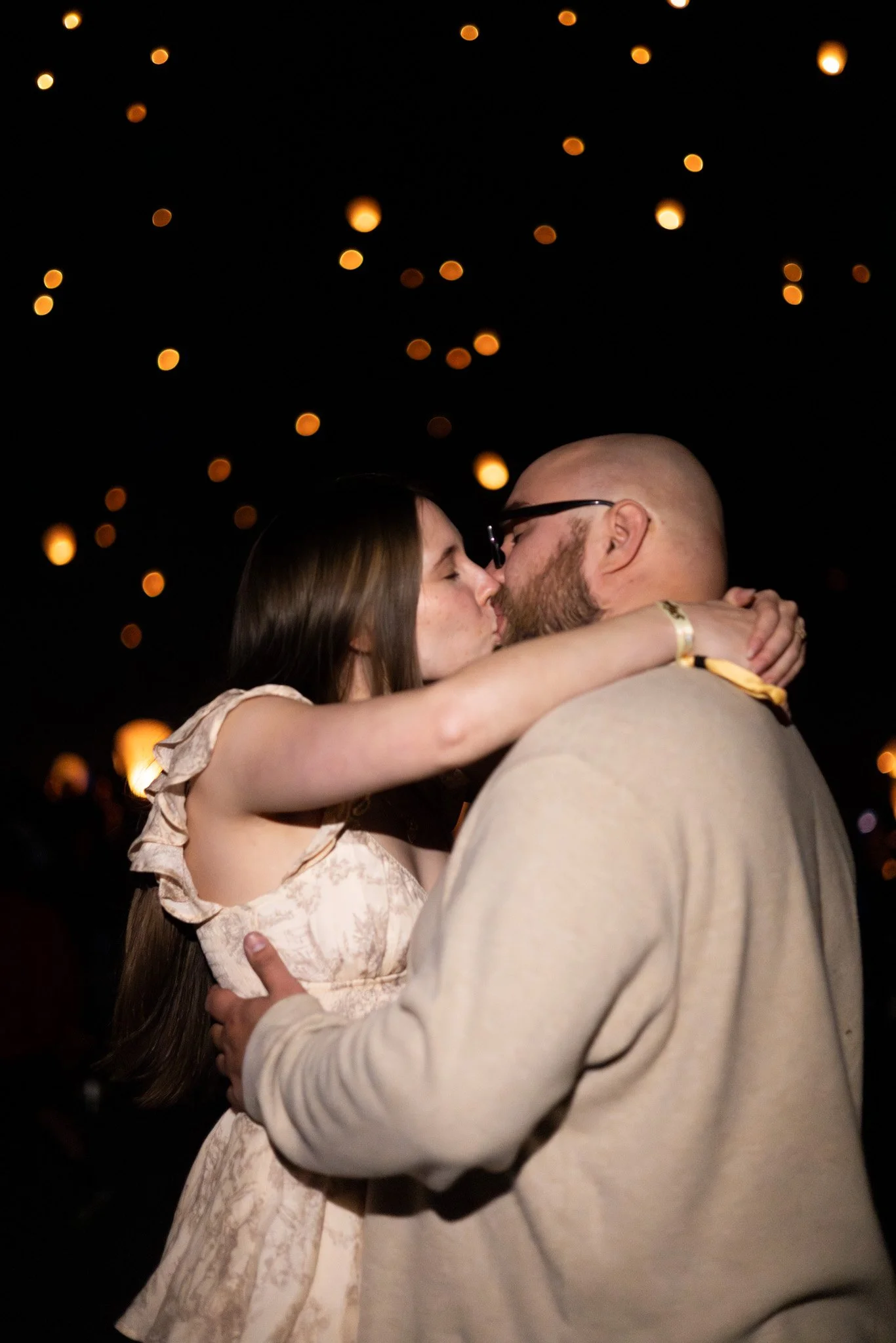 A couple passionately kissing at night, with warm bokeh lights in the background.